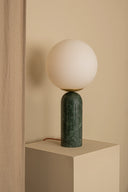 Table lamp with a green marble base and white spherical shade on a beige surface.