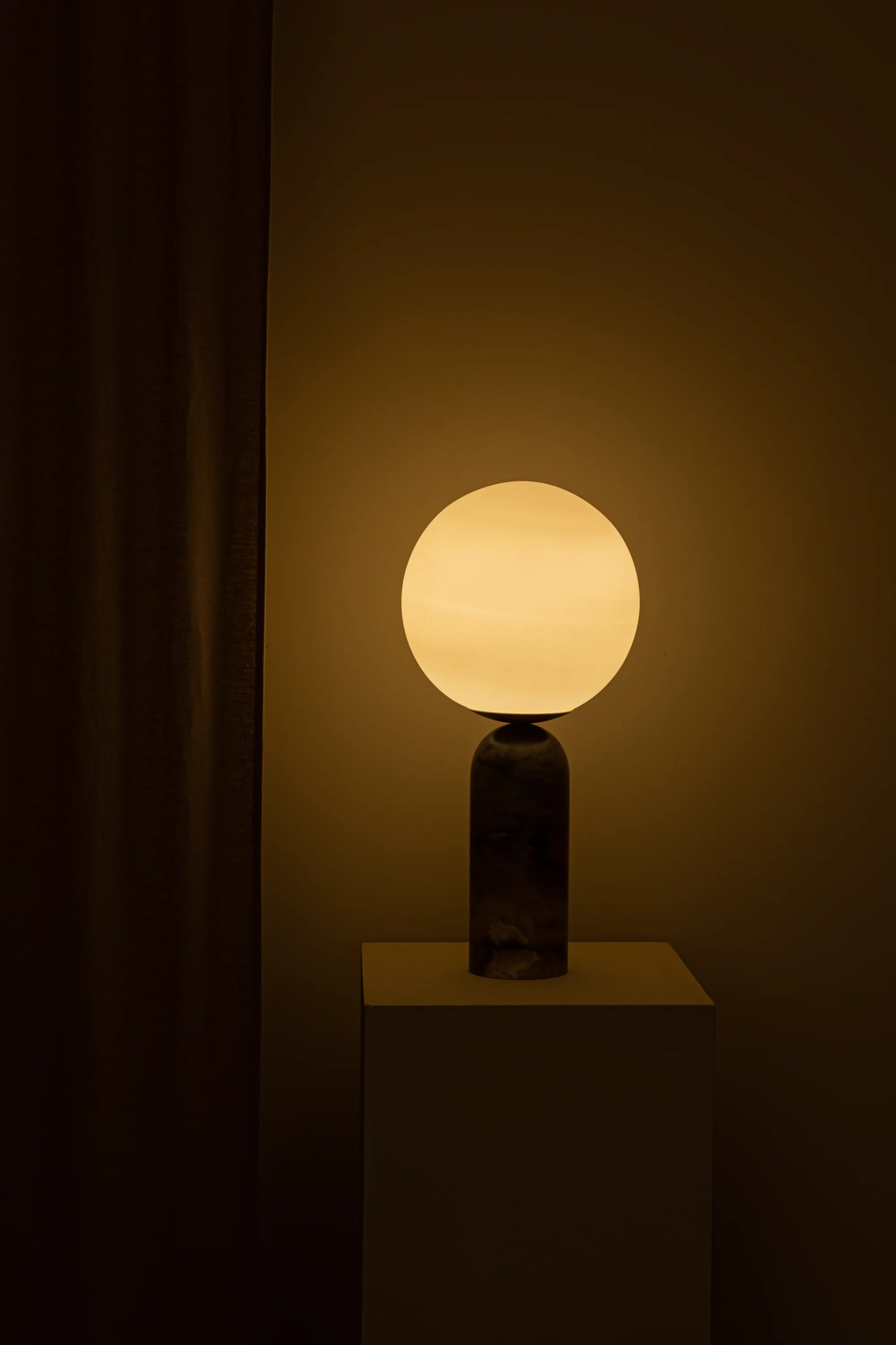 Table lamp with a spherical glass shade on a dark pedestal against a dark background