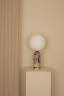 Modern lamp with marble base on a pedestal against a beige wall