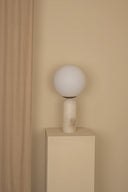 Spherical lamp on a pedestal against a beige wall with wooden paneling.