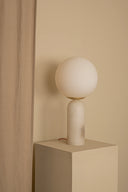 Minimalist table lamp with spherical shade on a beige cube against a beige wall.