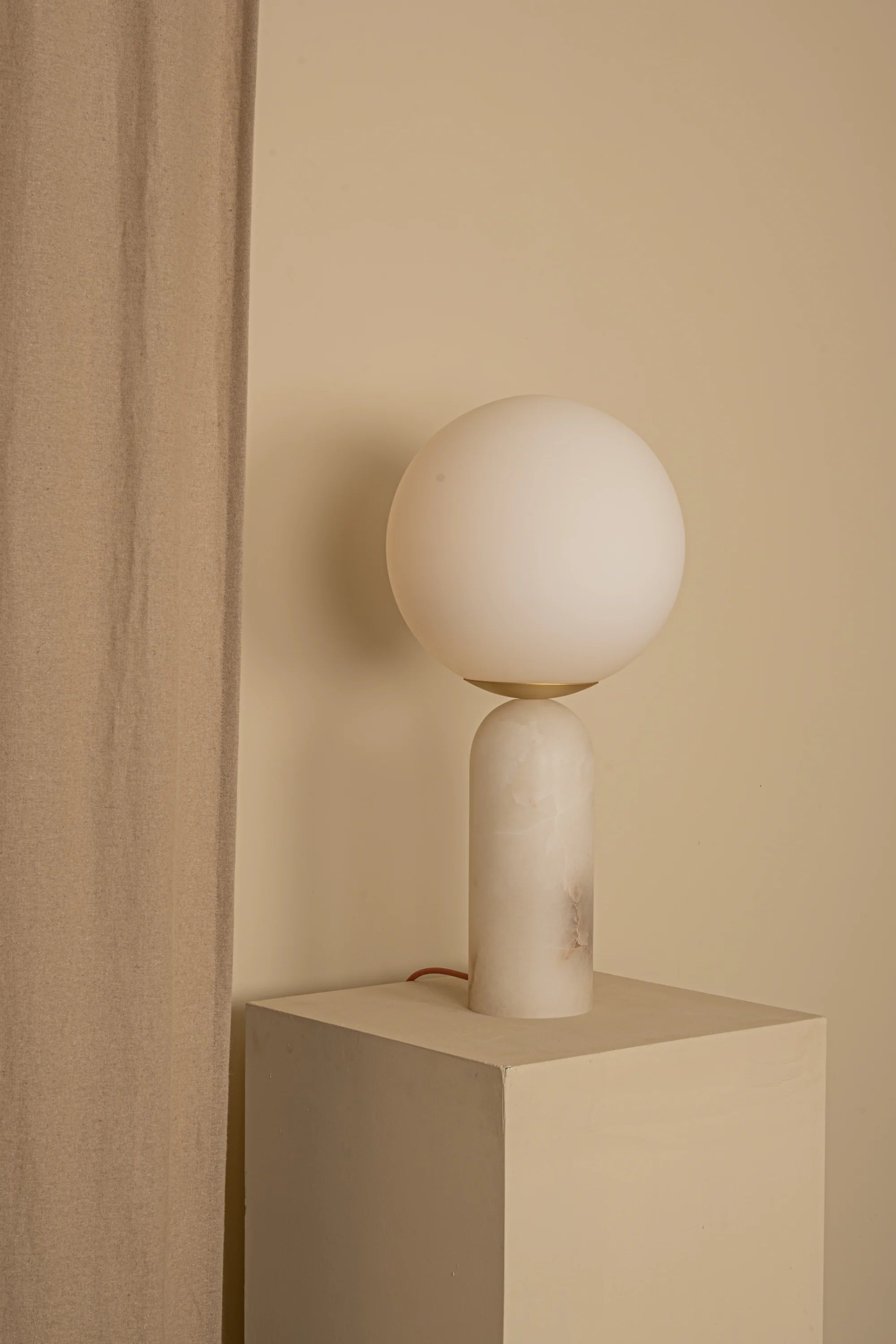 Minimalist table lamp with spherical shade on a beige cube against a beige wall.