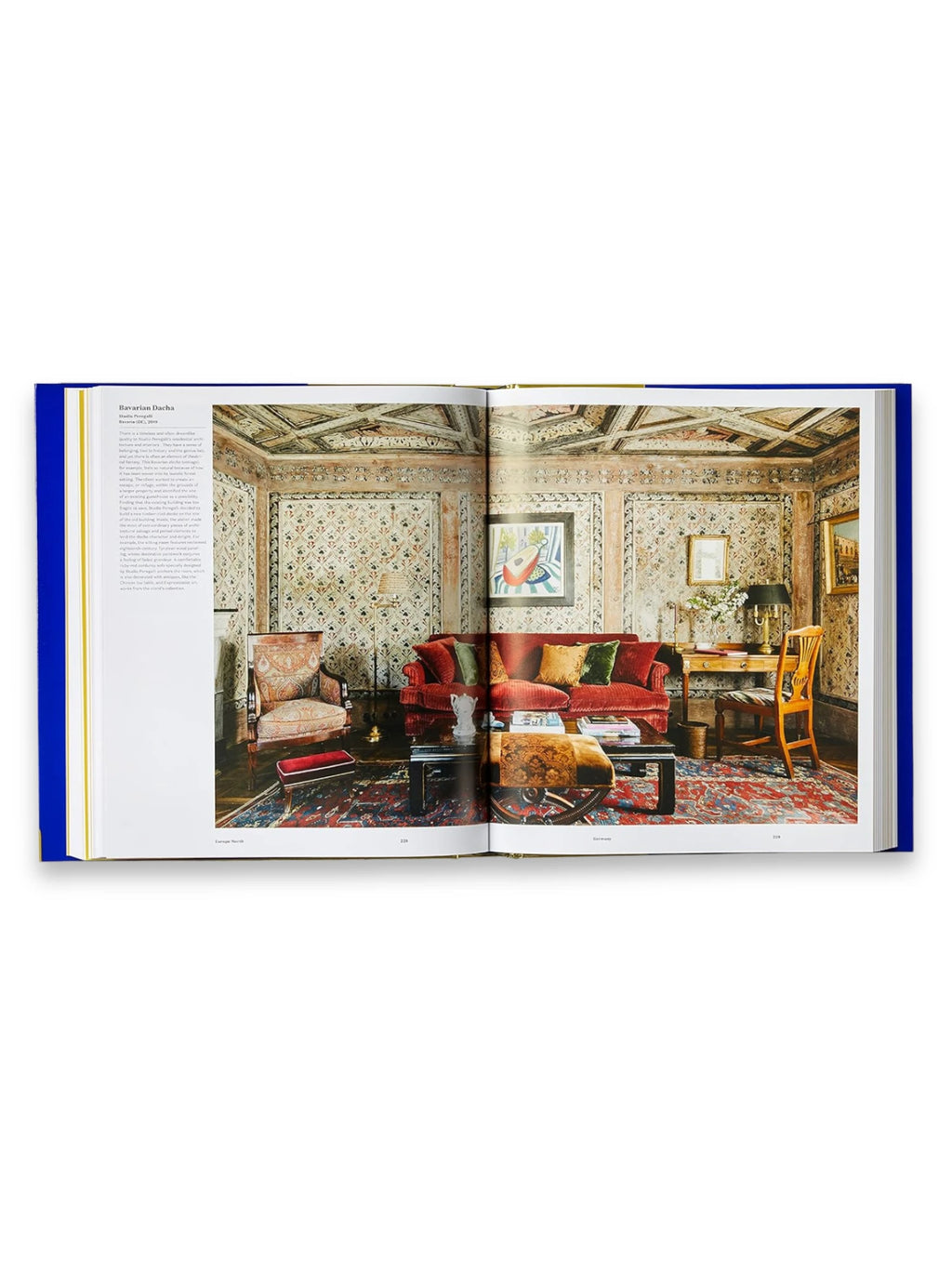 Book Atlas of Interior Design, an open, richly illustrated hardcover book showcasing a luxurious, intricately patterned living room with a red velvet sofa, ornate armchair, and patterned wallpaper. This premium design book provides inspiration for interior designers and home decor enthusiasts seeking elegant, global styles.
