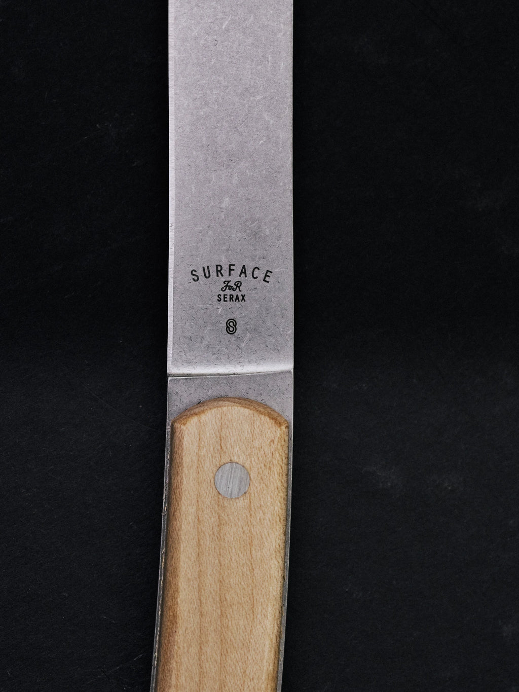 Serax Surface Steak Knife - Set of 4, a close-up showing the brushed stainless steel blade with "SURFACE FOR Serax S" engraving and a light natural wood handle secured by a silver rivet. This premium steak knife is perfect for discerning home cooks and hosts who value durable, stylish cutlery for their dining experiences.