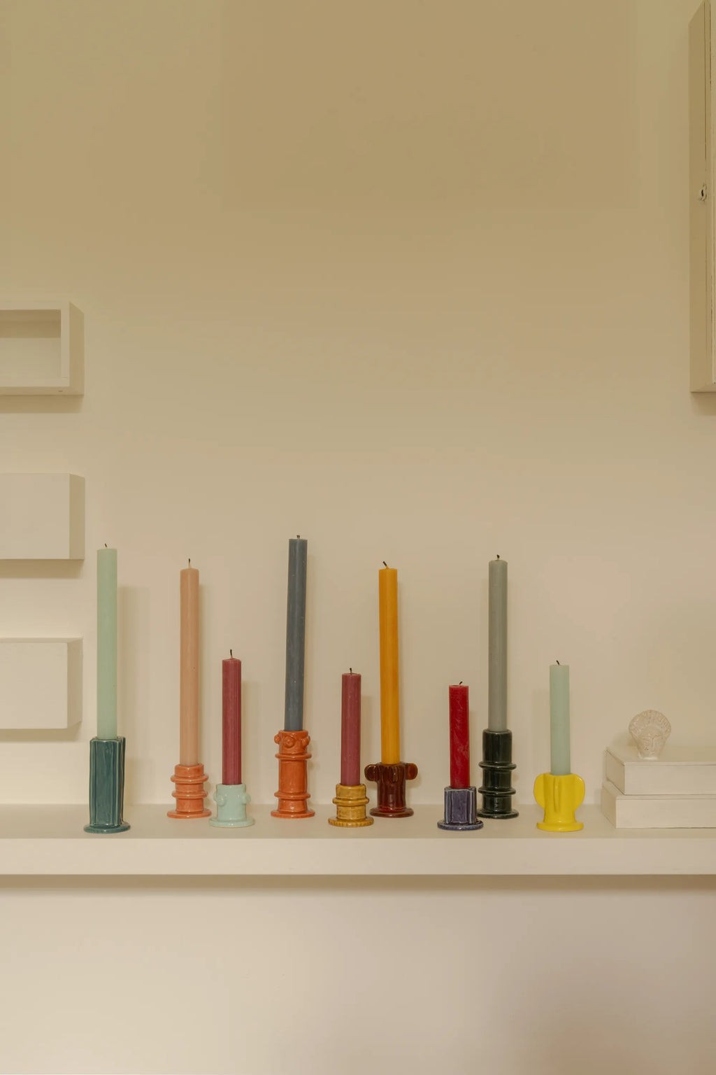 Serax Glazed Molly Candle Holder 01 - Set of 3, featuring a variety of colorful, glossy ceramic candle holders in different shapes and heights, arranged with assorted taper candles on a minimalist white shelf. These stylish and decorative candle holders are perfect for adding a touch of modern elegance to any home decor, ideal for design-conscious individuals.