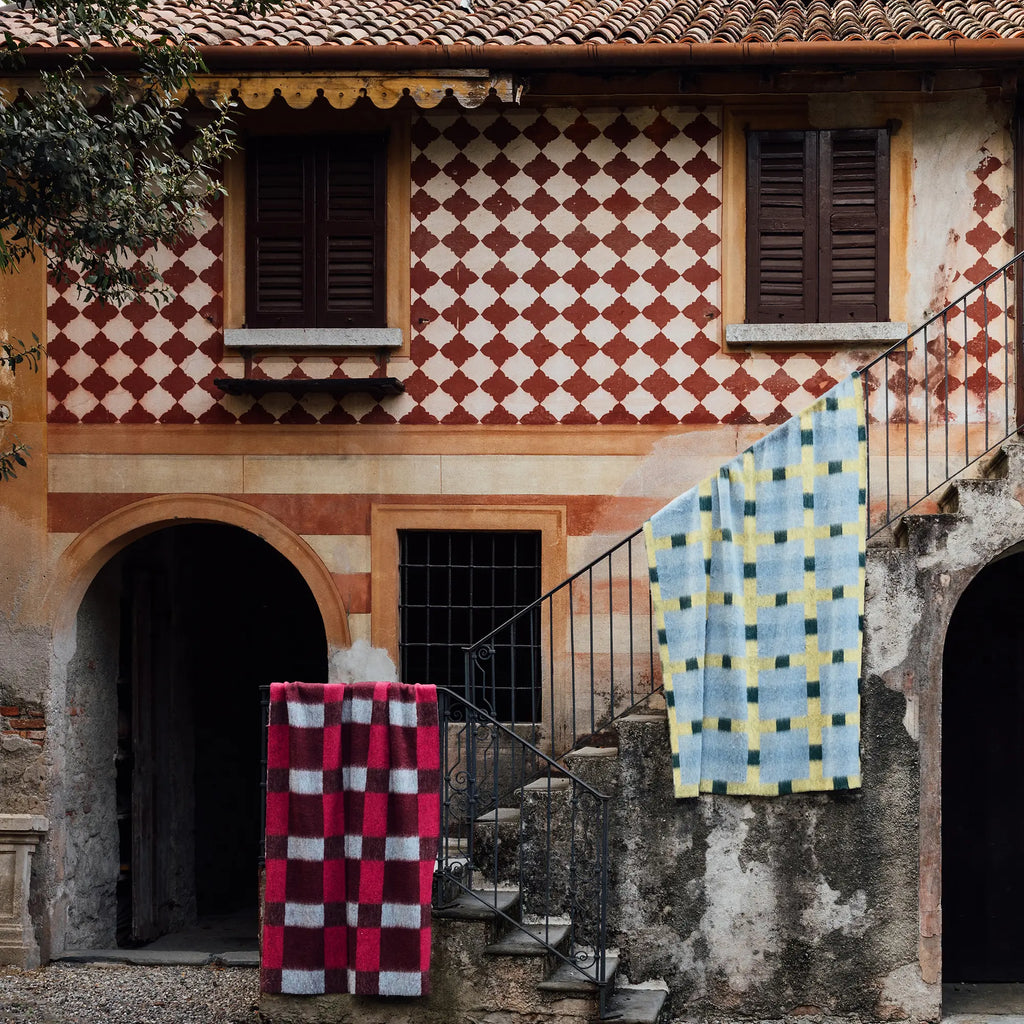 Layered Dancing Doll Oversized Throw Blanket, featuring a vivid blue, yellow, and green geometric check pattern on a soft, plush fabric, draped over an outdoor staircase railing. Perfect for adding...