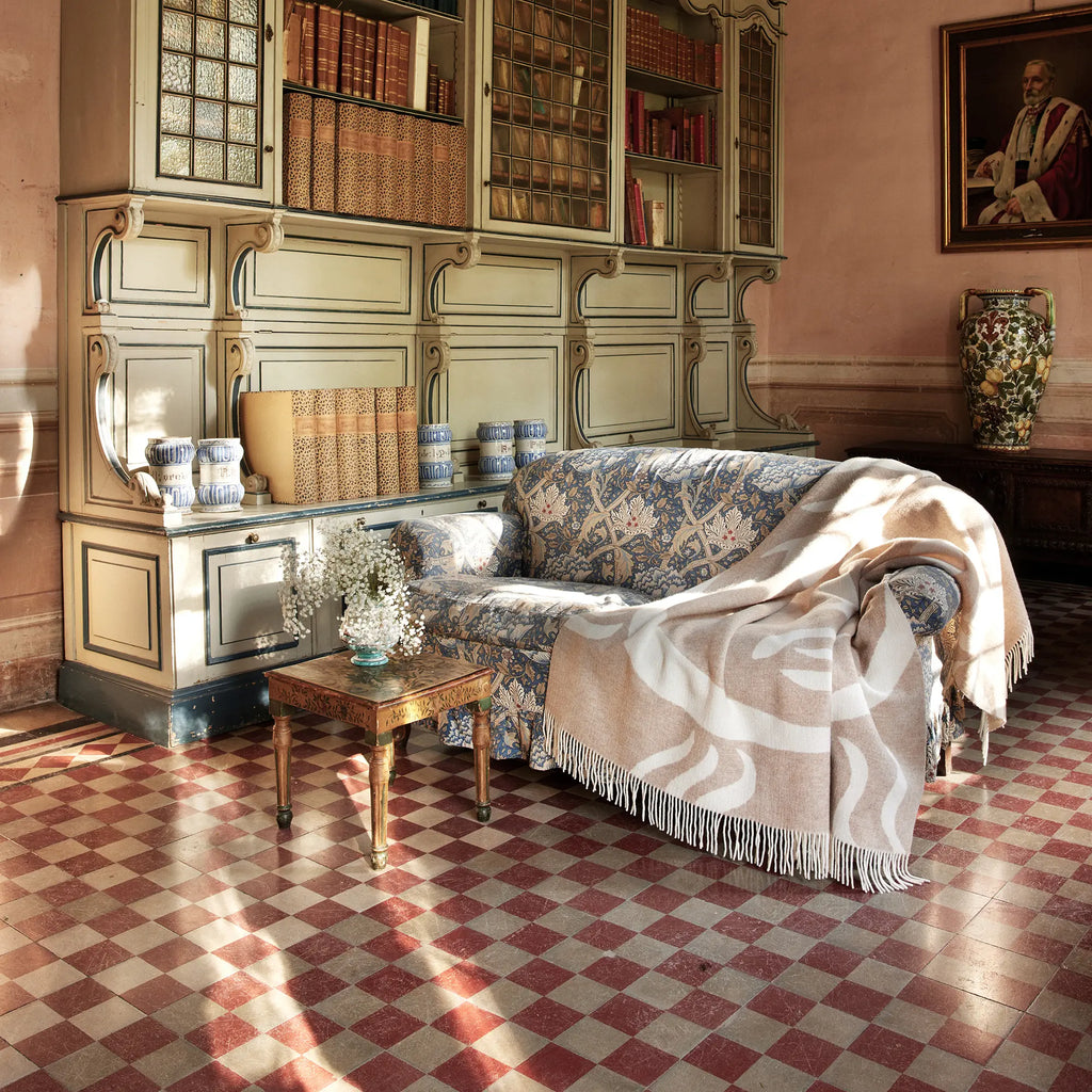 Layered Leggero Throw Blanket. A soft, light beige and white patterned throw blanket with fringe, draped over a blue floral sofa in a sunlit room. Perfect for adding a cozy, decorative touch to any...