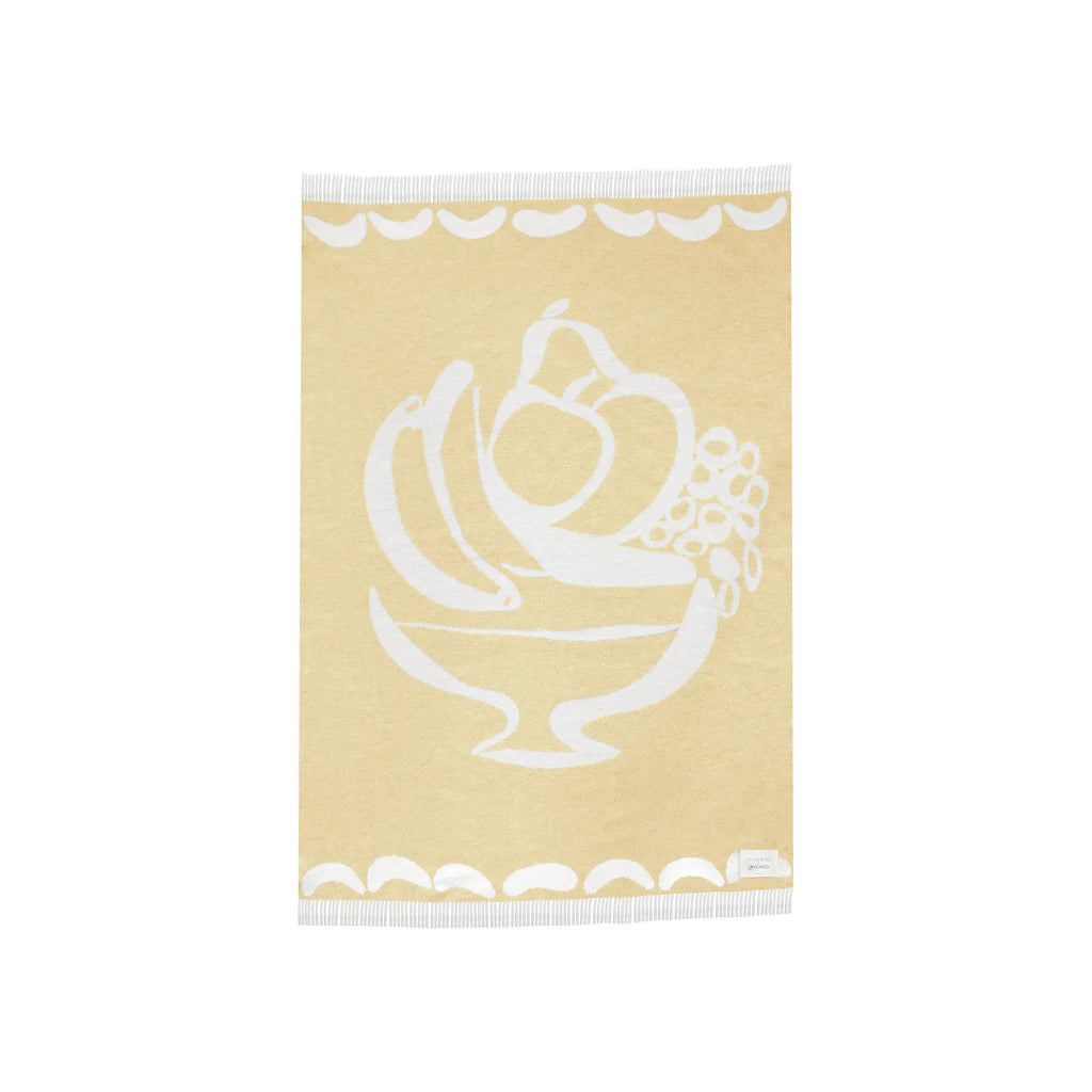 Layered Fruttato Throw Blanket, a soft cream-colored decorative throw with a large white fruit bowl design and fringe edges. Perfect for adding a cozy, artistic touch to any living space or bedroom.