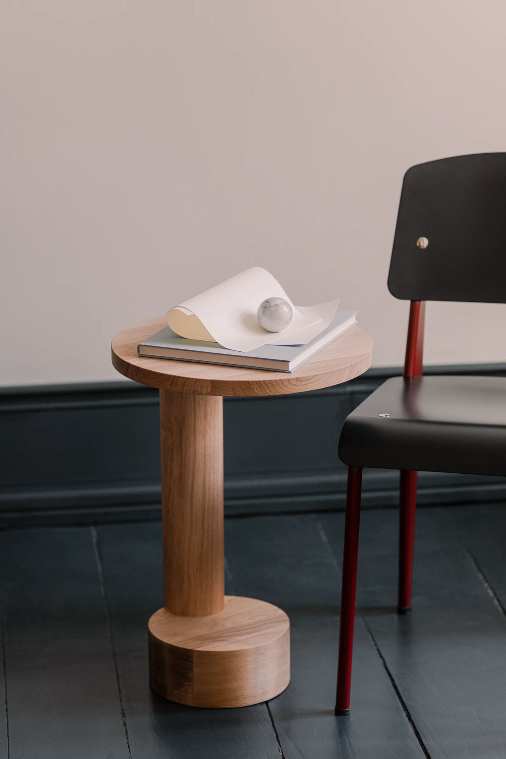 TAMO Bold Side Table, showcasing a solid light brown oak wood cylindrical pedestal base and round tabletop with visible grain, styled with a book, paper, and a grey marble sphere. A premium, authentic home accent.