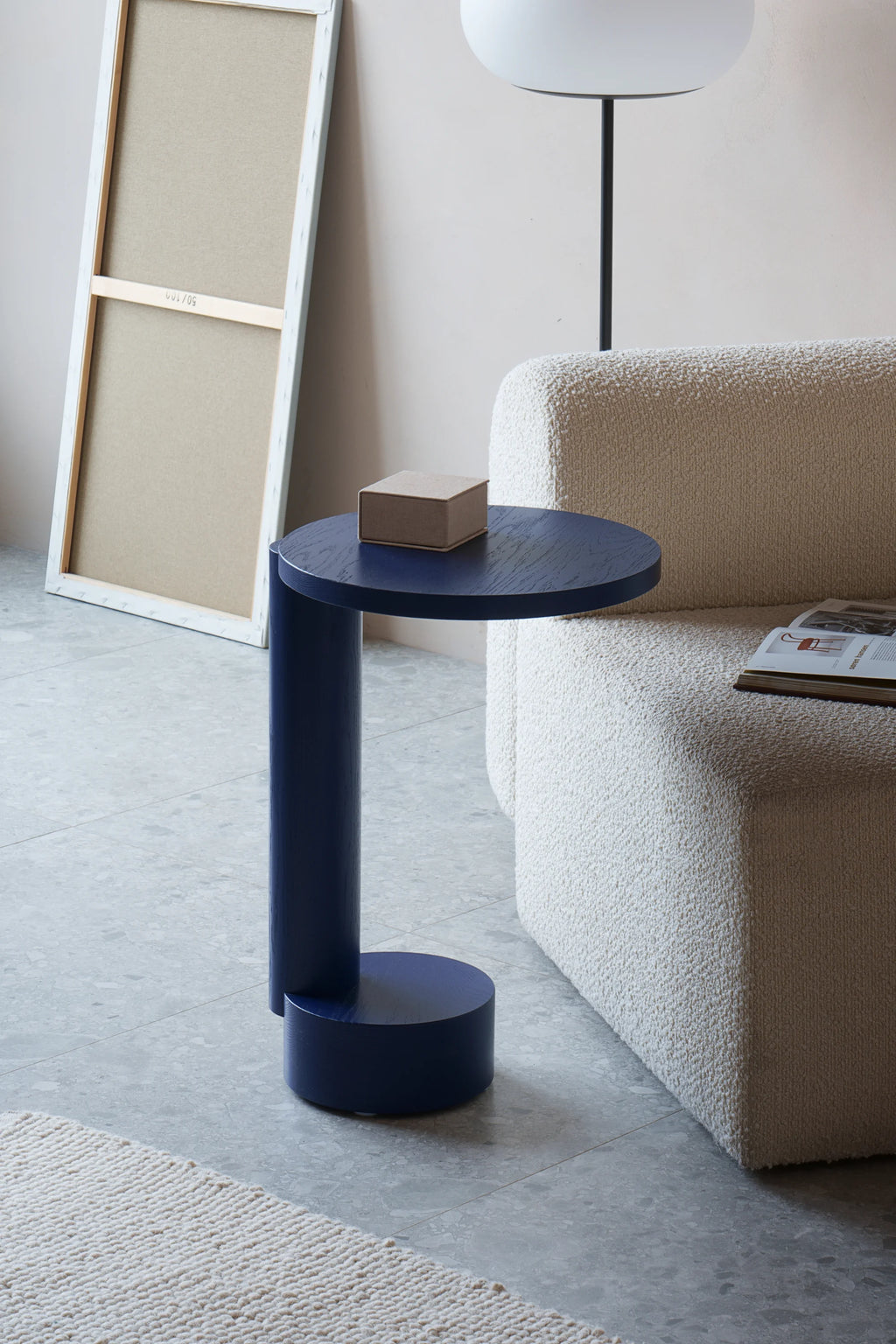 TAMO Bold Side Table, displayed as a navy blue C-shaped wooden accent table with a cylindrical base and round top in a modern living space. This designer side table is perfect for contemporary decor.