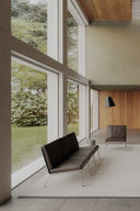 Modern interior with a large window view of greenery, featuring a black sofa and chair.