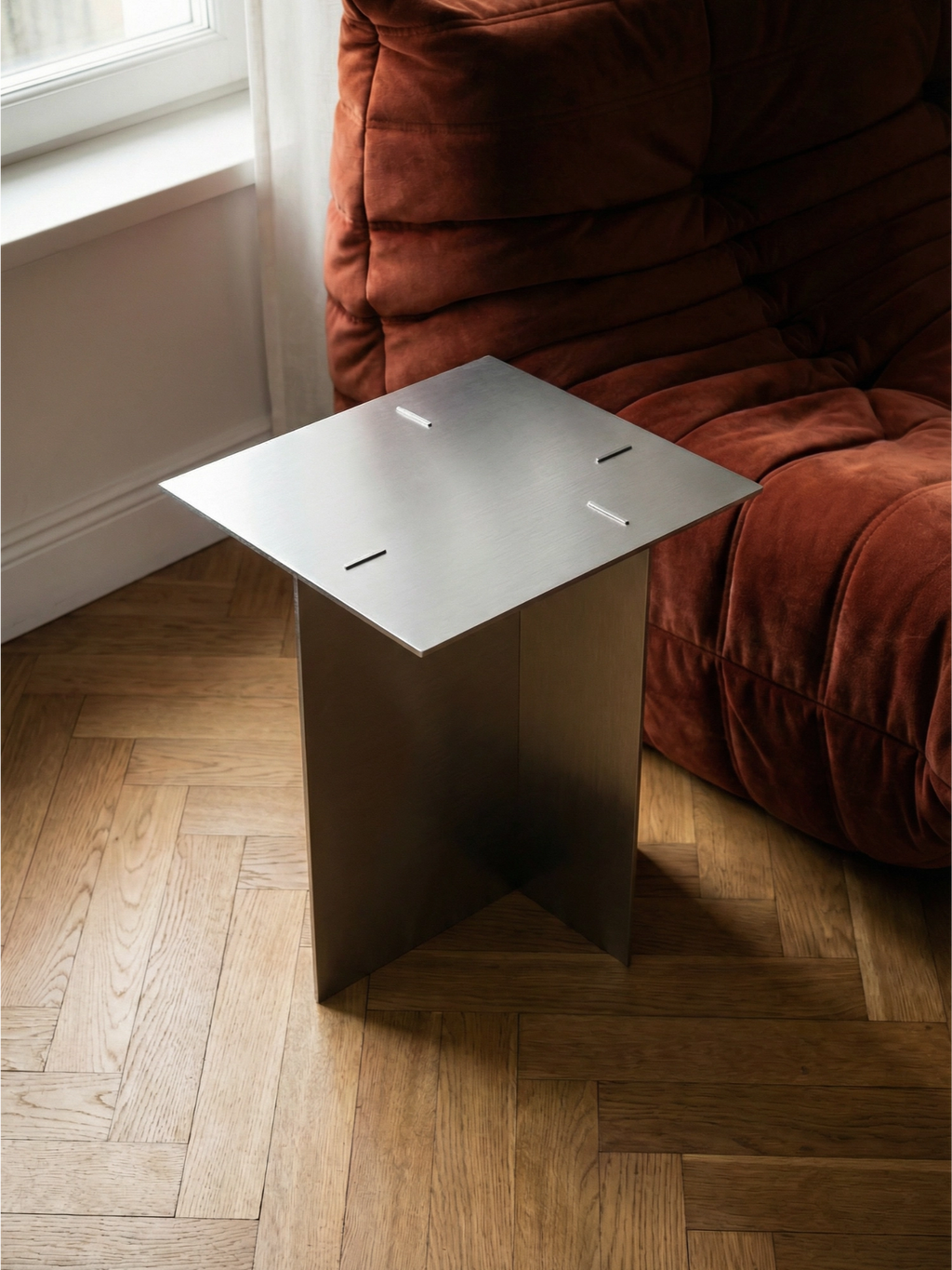 TCL Studios Bauhaus Side Table, a sleek minimalist side table crafted from brushed stainless steel with a subtle silver-grey metallic finish. Its striking geometric design features a clean square tabletop and a sturdy cross-shaped base, embodying an industrial chic aesthetic. This contemporary accent table is perfect for modern living rooms, as a stylish bedroom side table, or for minimalist home office decor.