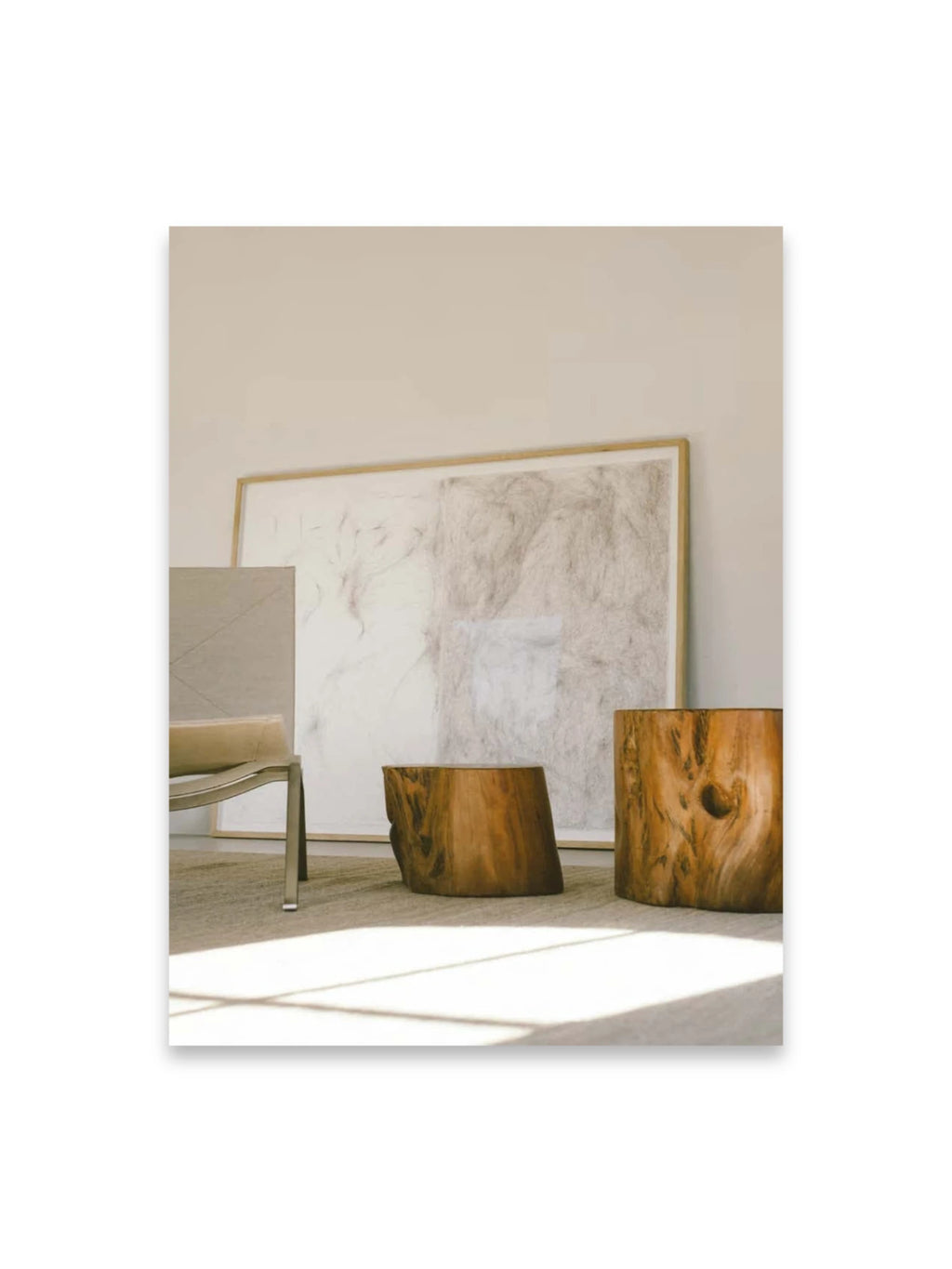 Book Bea Mombaers – items & interiors, featuring a modern interior scene with two rustic wooden tree stump side tables, a contemporary light gray upholstered armchair with a metal frame, and a large framed abstract artwork leaning against a light beige wall. This stylish design book is perfect for interior design enthusiasts seeking modern and natural decor inspiration.