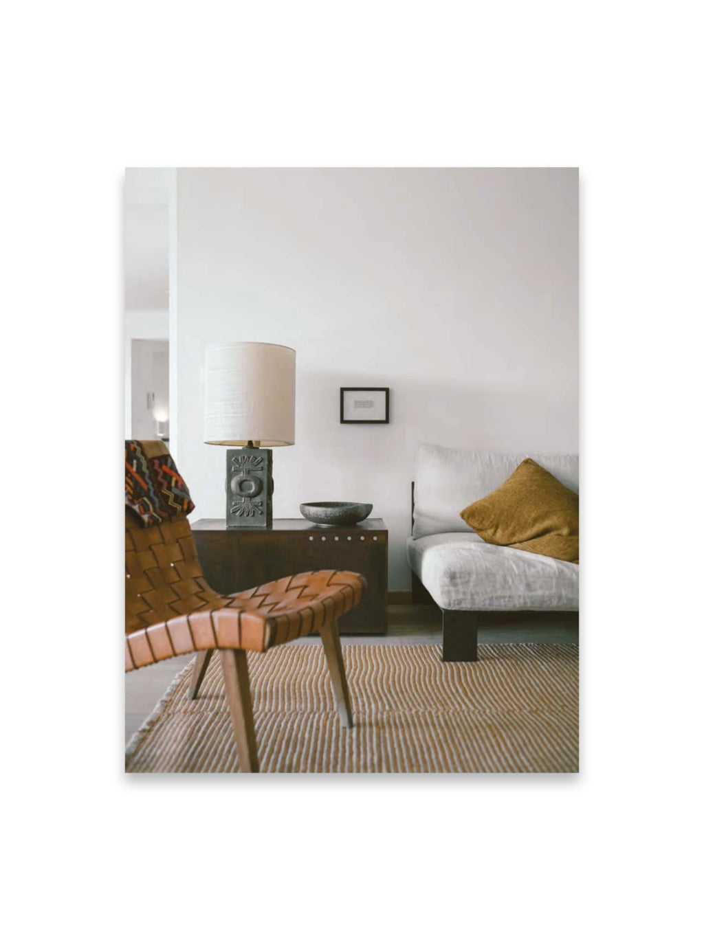 Book Bea Mombaers – items & interiors, featuring a cozy, stylish living room interior with a light woven leather chair, a textured white sofa with a mustard yellow pillow, and a dark wooden side table with a decorative lamp. This elegant book is perfect for interior design enthusiasts and home decor inspiration seekers.