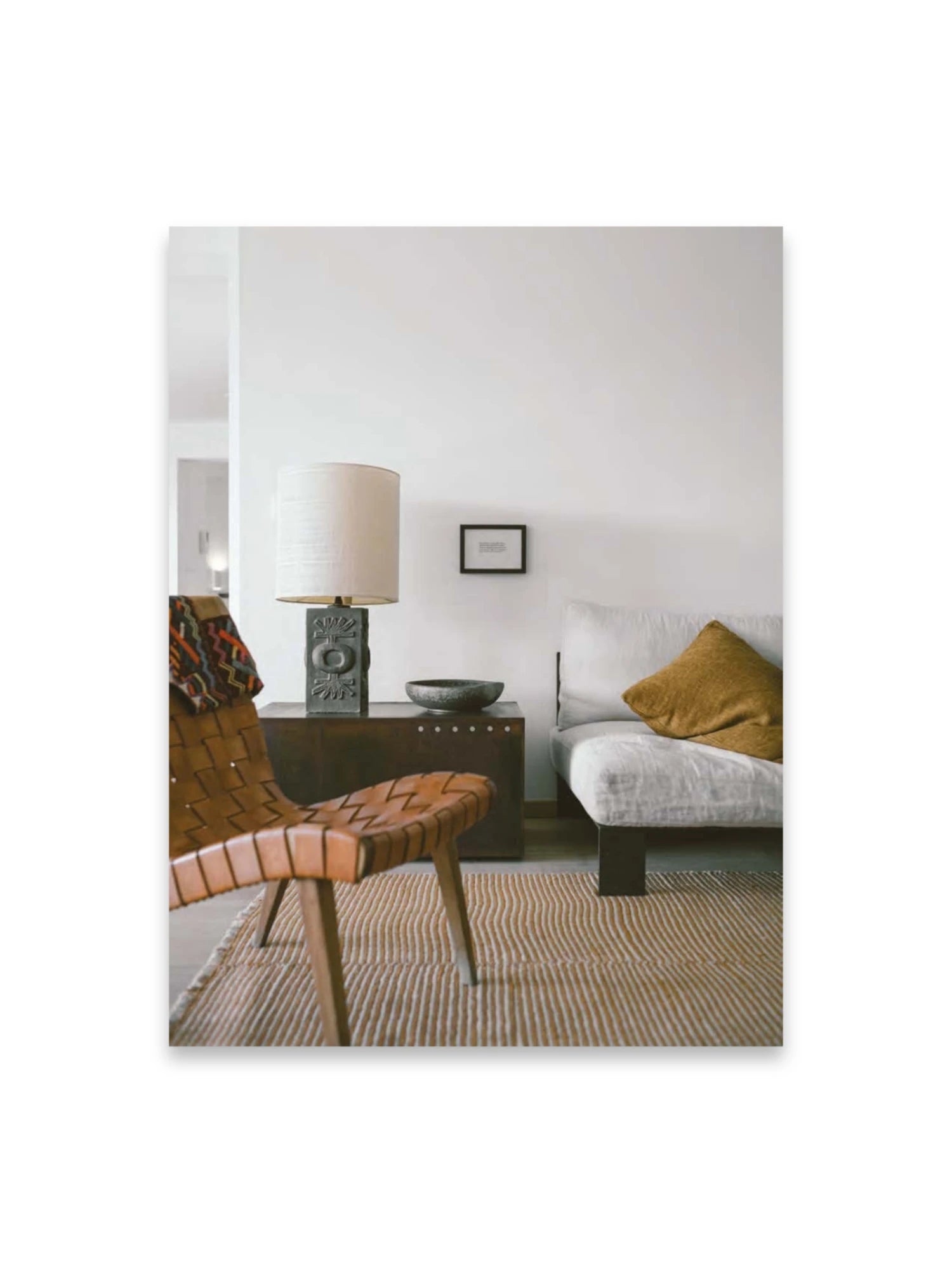 Book Bea Mombaers – items & interiors, featuring a cozy, stylish living room interior with a light woven leather chair, a textured white sofa with a mustard yellow pillow, and a dark wooden side table with a decorative lamp. This elegant book is perfect for interior design enthusiasts and home decor inspiration seekers.