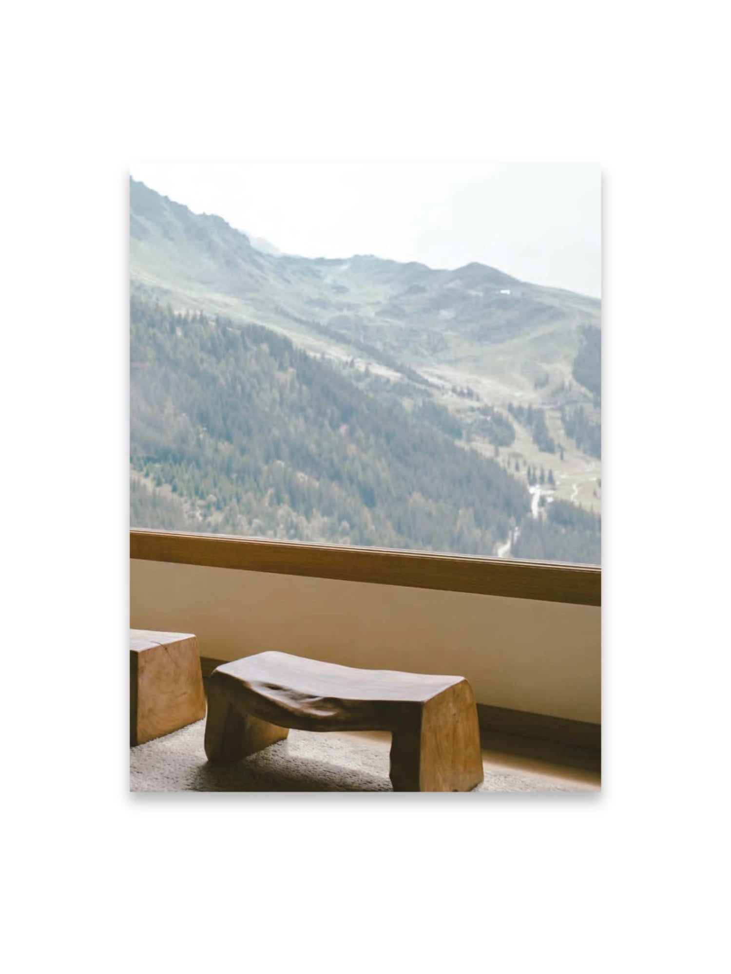 Book Bea Mombaers – items & interiors, featuring a natural light wood stool with organic curves and a square wooden block, set against a stunning mountain landscape with pine forests and hazy peaks visible through a window. This luxury interior design book is perfect for decor enthusiasts seeking inspiration for elegant, nature-inspired spaces.