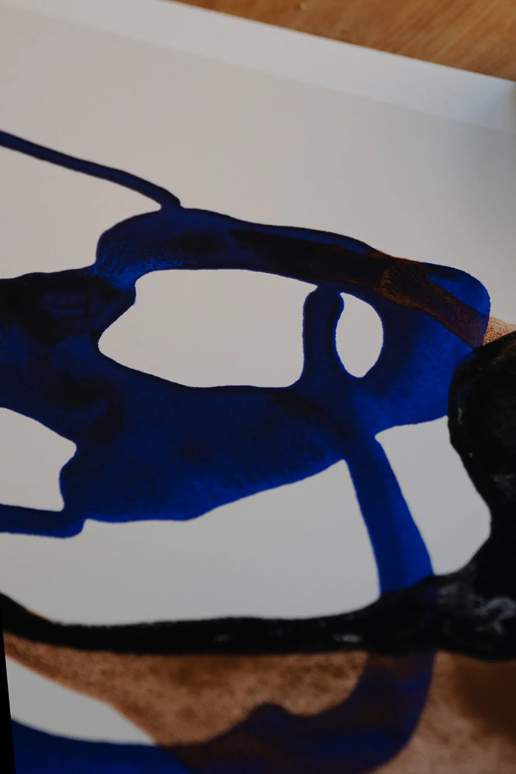 The Poster Club Float, an abstract art print featuring organic, fluid shapes in rich royal blue, deep black, and earthy brown tones that appear to float across a crisp white background. This contemporary wall art piece offers a dynamic blend of color and form with a subtle textured appearance. Ideal for adding a sophisticated touch to modern living rooms, bedrooms, or gallery walls.