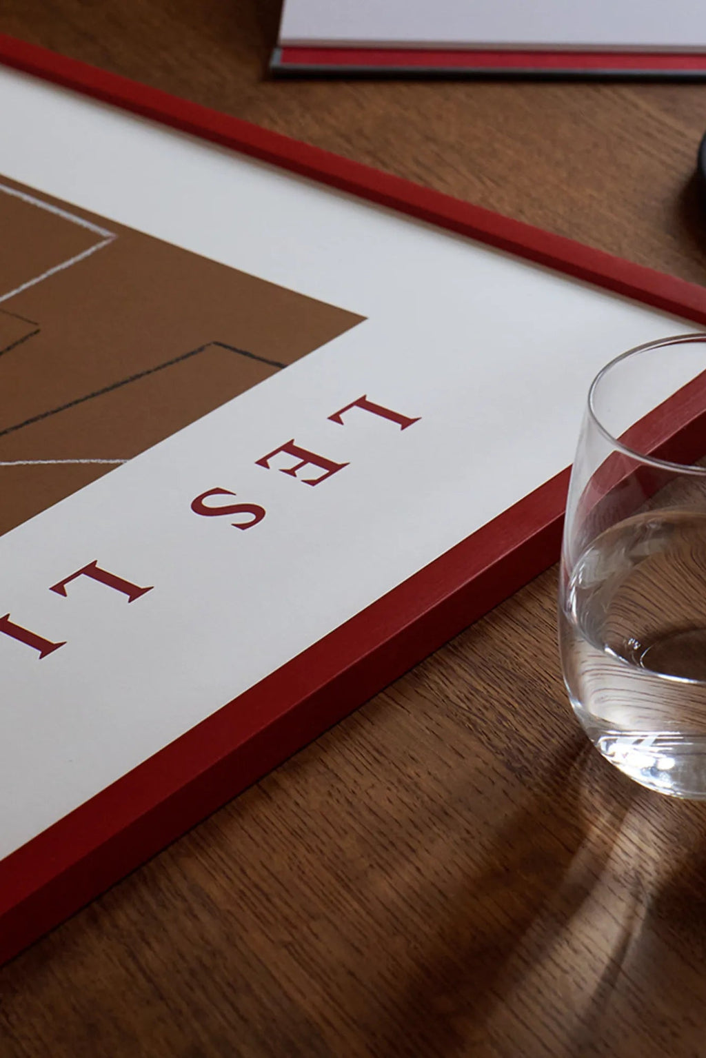 The Poster Club Les Lignes, a contemporary abstract art print featuring a bold brown geometric shape with fine black lines on a crisp white background, complemented by elegant red serif typography.
