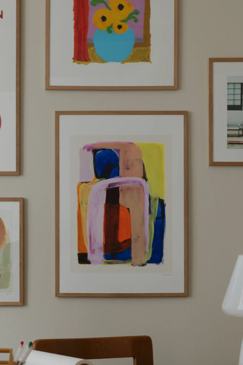The Poster Club Prana, a vibrant abstract art print featuring bold, expressive brushstrokes in a rich palette of blues, oranges, yellows, purples, and pinks, creating an organic, layered composition. This modern abstract poster is beautifully presented with a white mat and a light natural oak frame, enhancing its contemporary aesthetic. Perfect as colorful wall art for a living room, bedroom, or home office, adding a dynamic focal point to any modern gallery wall.