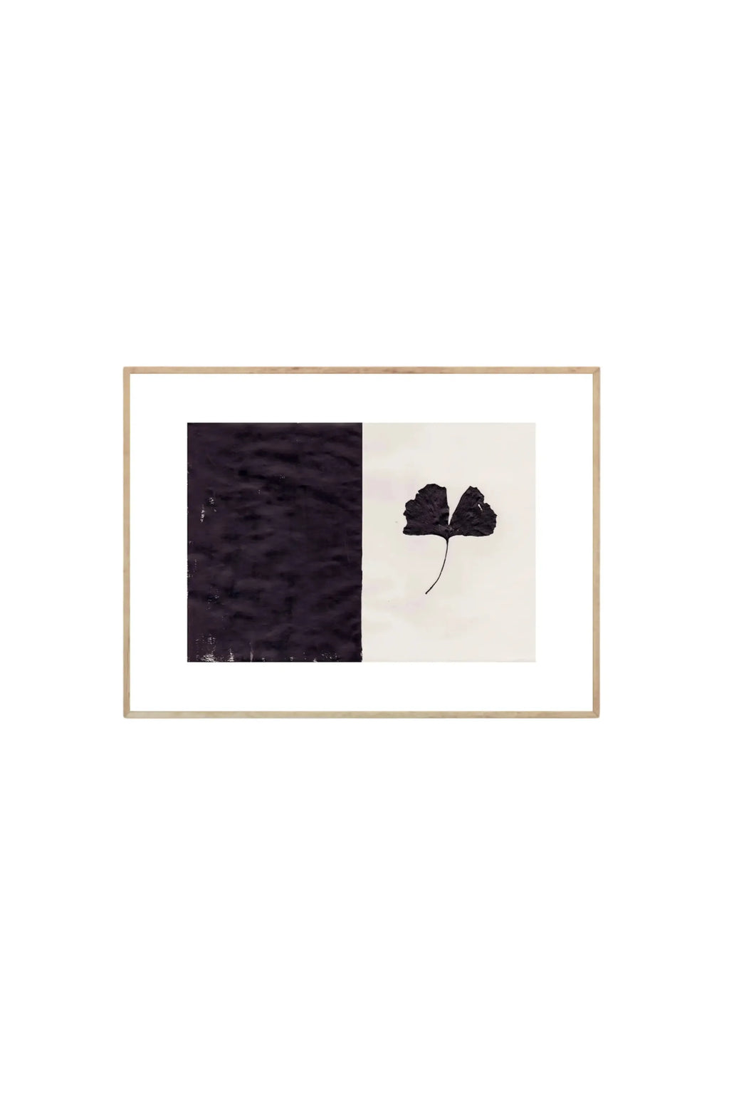 The Poster Club Black Ginkgo - Art Print, featuring a pressed, dark ginkgo leaf against a cream background, contrasted with a textured black block on the left, all within a thin natural wood frame. This elegant botanical poster is perfect for adding modern, minimalist wall decor to any stylish home or office.