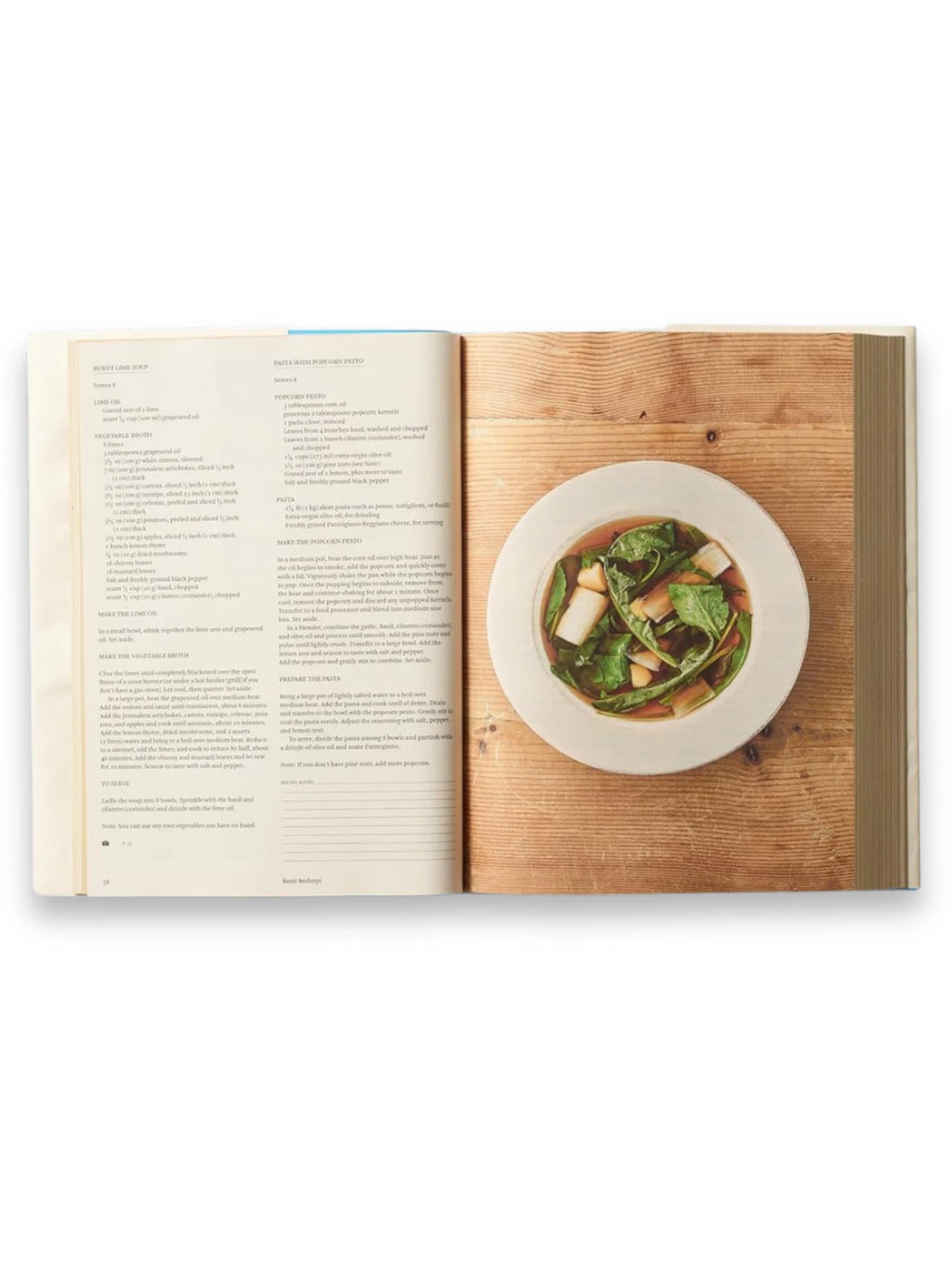 Book Bread is Gold: Extraordinary Meals With Ordinary Ingredients, an open hardcover cookbook showcasing a vibrant recipe for "Pasta With Popcorn Pesto" on the right page, accompanied by a beautifully styled white ceramic bowl of pasta on a rustic wooden surface. This insightful culinary book is perfect for home cooks seeking creative, sustainable recipes and cooking inspiration.