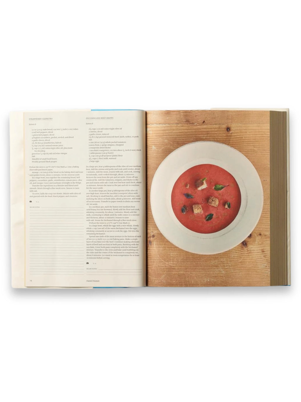 Book Bread is Gold: Extraordinary Meals With Ordinary Ingredients, an open cookbook displaying a vibrant red tomato soup with croutons and basil in a white bowl on a rustic wooden background, alongside detailed recipes for "Strawberry Gazpacho" and "Zucchini and Beef Gratin." This inspiring culinary guide is perfect for home cooks seeking creative, budget-friendly recipes.