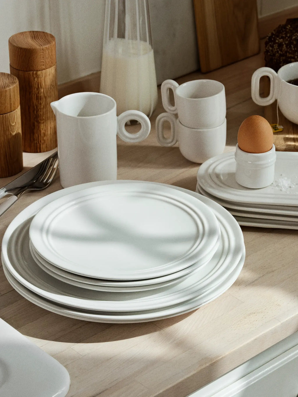 Broste Copenhagen Stevns Dinner Set for 4, an off-white stoneware dinnerware collection featuring round dinner plates and side plates with subtle concentric ring details, alongside matching mugs and a pitcher with distinctive organic loop handles. This modern minimalist ceramic set provides elegant Scandinavian tableware for everyday kitchen use or contemporary dining room settings.