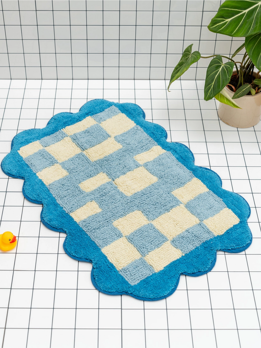 TARTA GELATINA Burbuja Bath Mat, a playful tufted cotton bath mat featuring a retro-inspired checkerboard pattern in light blue and cream, framed by a vibrant scalloped border in bright blue. This soft, plush bathroom rug adds a fun, contemporary accent to any modern bathroom or kids' space.