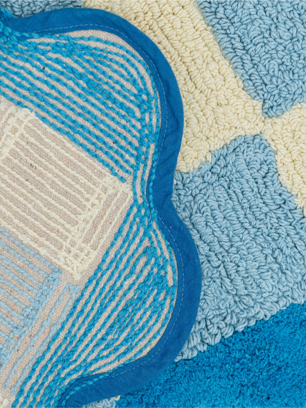 TARTA GELATINA Burbuja Bath Mat, a playful hand-tufted cotton bath mat featuring an organic scalloped shape with a vibrant royal blue fabric border. It showcases a rich, textured design in shades of bright blue, sky blue, cream, and beige, combining soft loop pile sections with striped flat-woven patterns.