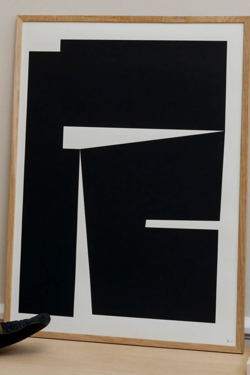 The Poster Club Composition 04, a modern minimalist abstract art print featuring bold black geometric shapes with sharp angles and clean lines against a crisp white background. This striking black and white print is presented in a light natural oak frame. Perfect as contemporary wall art for gallery walls, Scandinavian living rooms, or modern home offices.