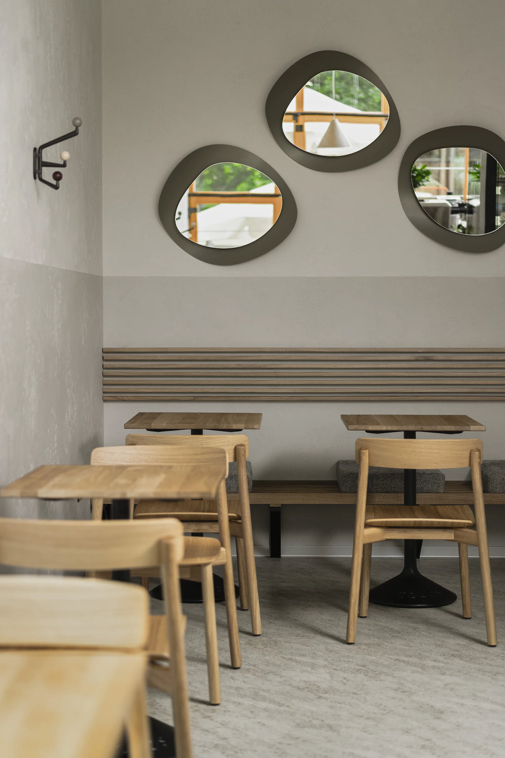 TAMO Arche Chair in light oak wood, featuring a curved backrest and woven seat, styled with matching wooden tables and subtle gray seat cushions in a modern cafe setting. Ideal for contemporary dining.
