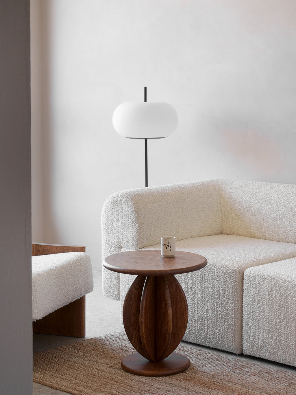 TAMO Citrus Side Table, featuring a round dark brown oak tabletop & unique carved spherical base, styled next to a cream boucle sofa. A statement modern furniture piece.