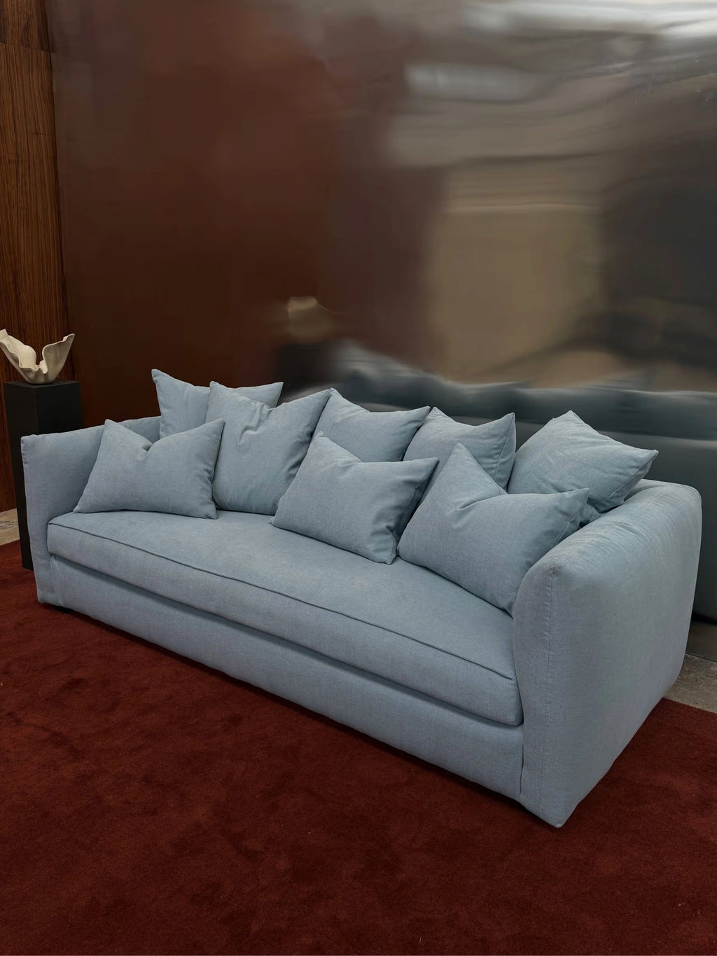 Tinted Objects Cornell Sofa, a luxurious light blue fabric sofa with multiple plush back cushions and a clean, modern design. This comfortable and stylish sofa is perfect for contemporary living rooms seeking elegant seating.