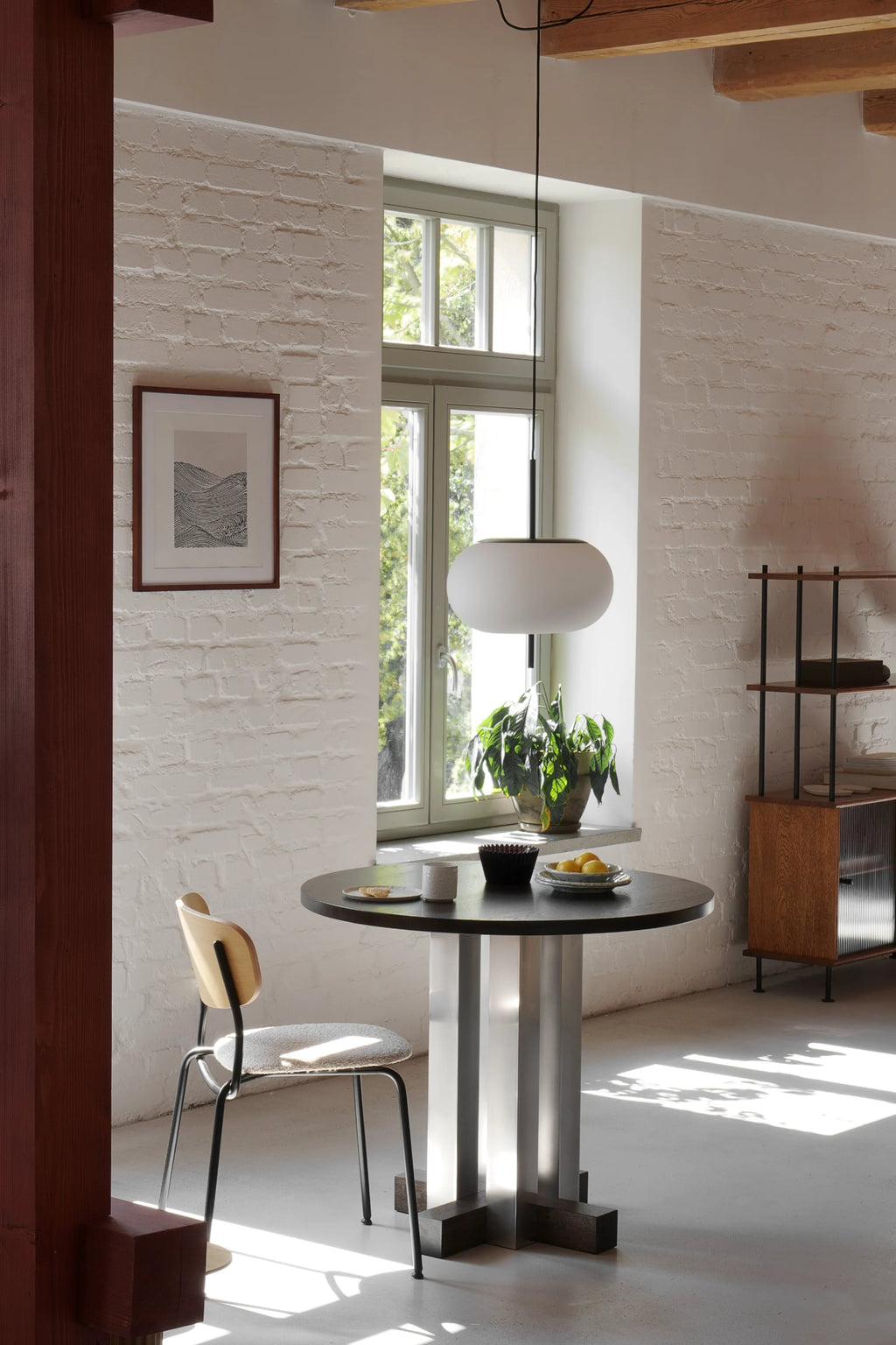 TAMO Cruz Round Table in a lifestyle shot. Features a premium dark wood top, unique fluted silver/gray metal pedestal base, and dark wood cross supports. Ideal for modern dining.