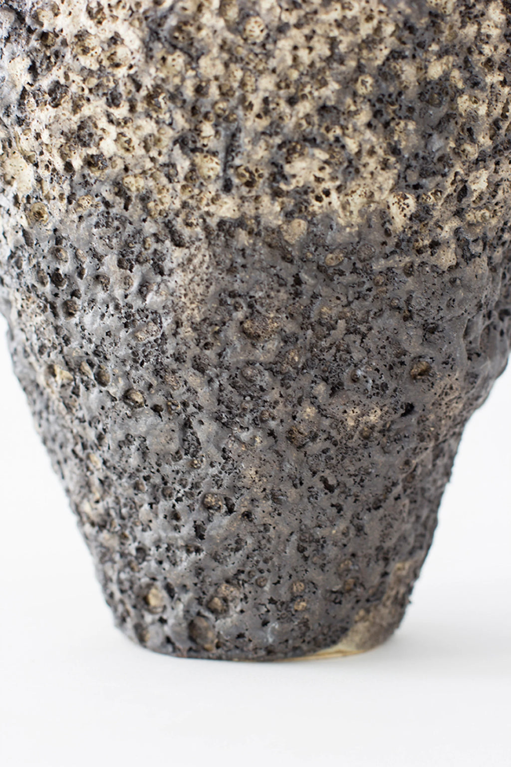 Canoa Lab Arq 001 Vase, a close-up of the base revealing the deeply textured, dark gray and black volcanic-like ceramic material, emphasizing its rugged and earthy design, displayed on a white background.