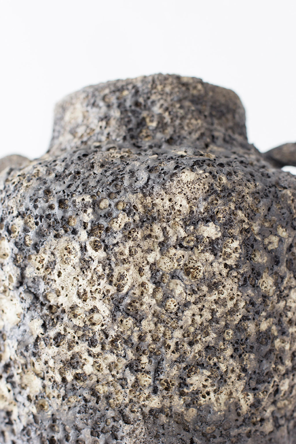 Canoa Lab Arq 001 Vase, a detailed view of the upper body, showcasing the rich, porous texture of the dark ceramic material and the subtle variations in its gray and black tones, on a white background.