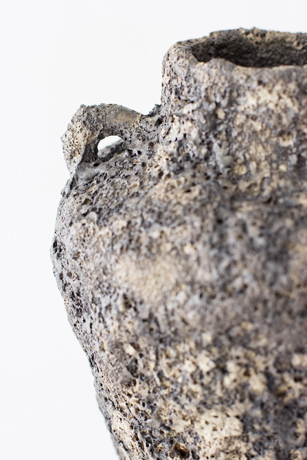 Canoa Lab Arq 001 Vase, a side view highlighting one of its small, integrated handles and the intricate, rough texture of the dark, volcanic-inspired ceramic surface, presented on a white background.