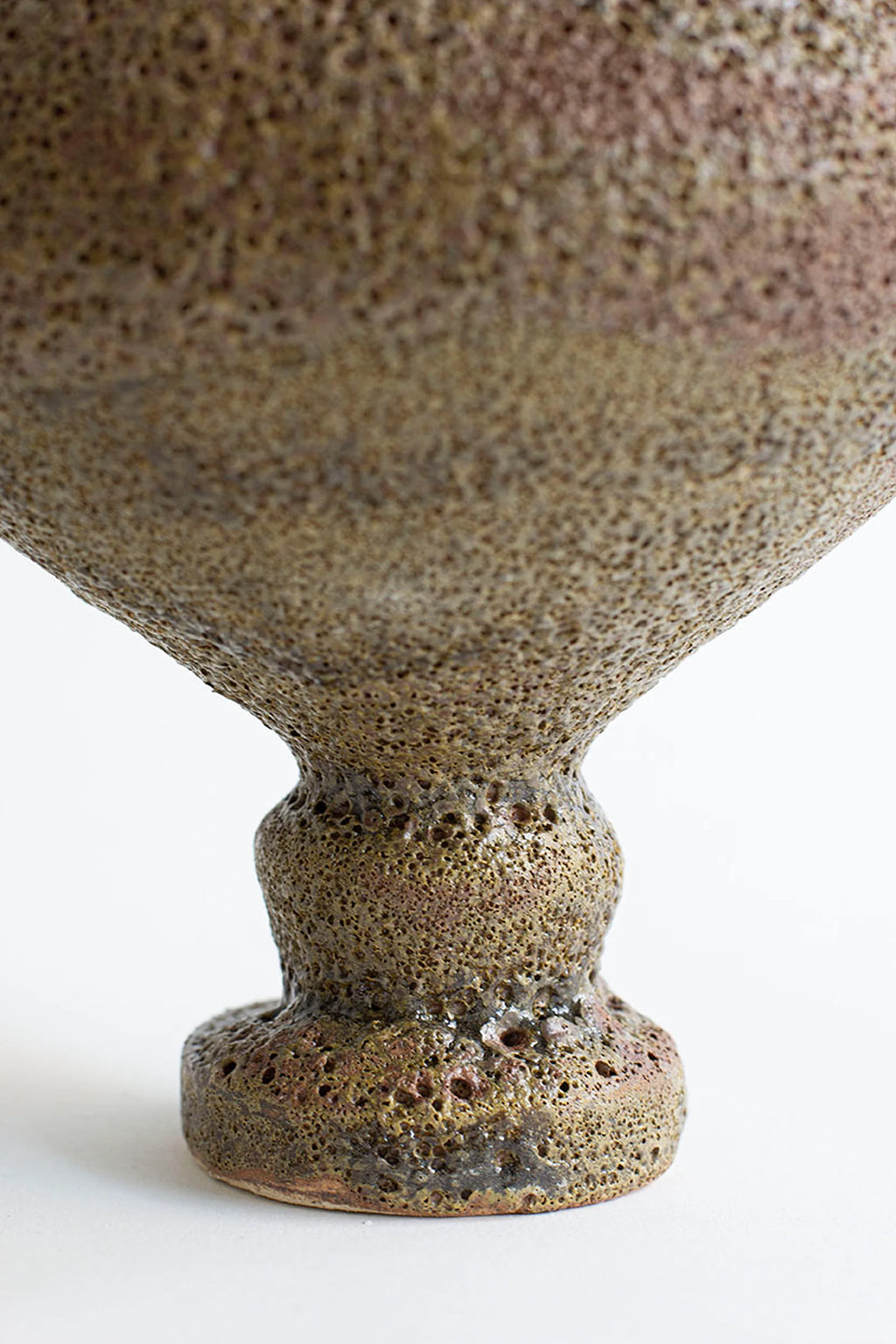 Canoa Lab Arq 002 Musgo Vase, a handcrafted ceramic vase featuring a rich moss green and brown volcanic textured finish with deep pores and a rustic, organic silhouette. This unique artisanal stoneware piece brings a wabi-sabi aesthetic to modern minimalist living rooms or natural-inspired shelf styling.