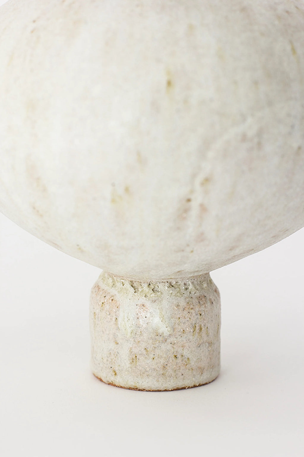 Canoa Lab Arq 005 Vase, a detailed shot of the vase's base, showcasing the textured, matte off-white ceramic material with subtle speckles and a sturdy, cylindrical design, on a white background.