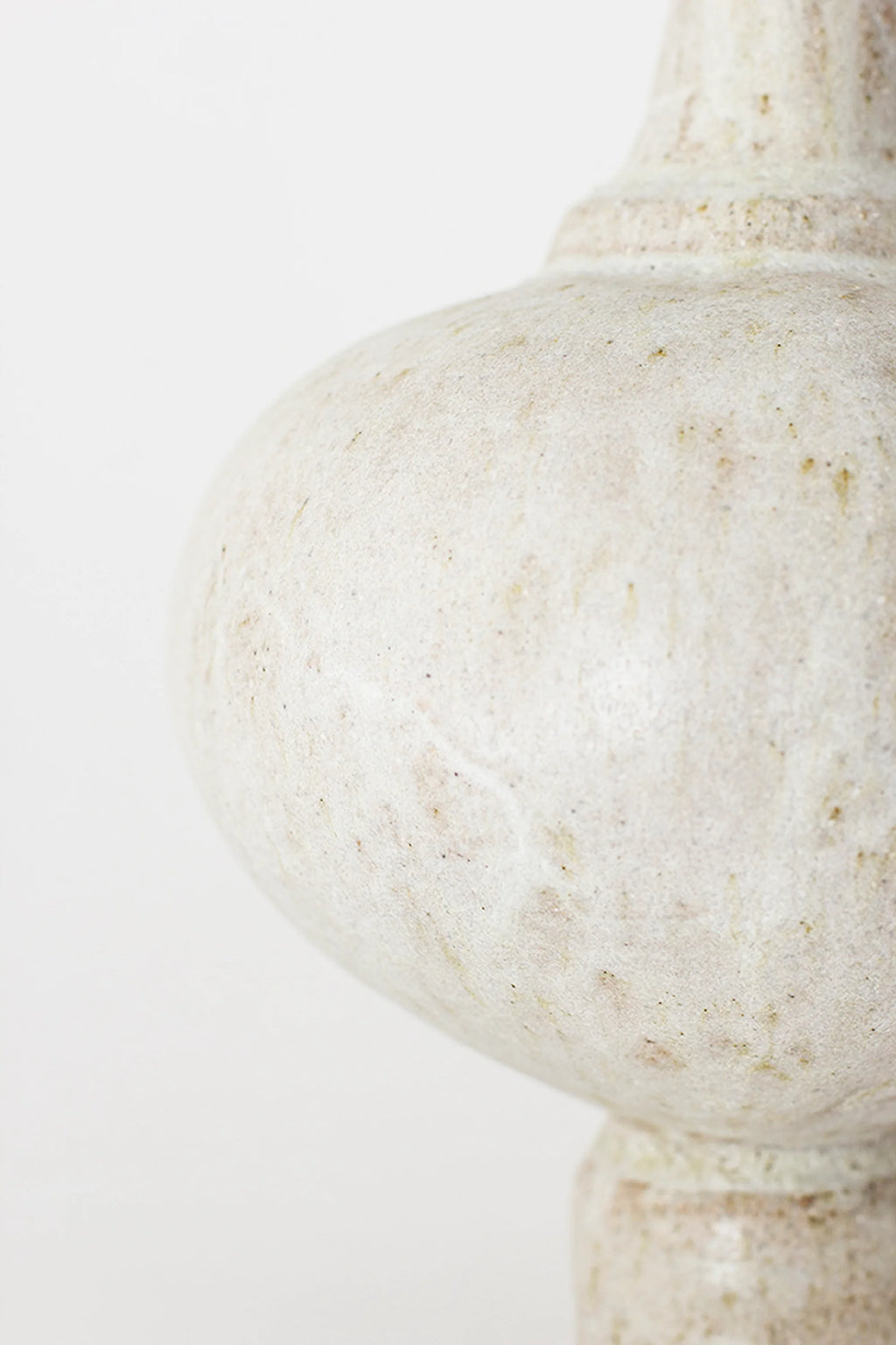 Canoa Lab Arq 005 Vase, a close-up side view of the round, bulbous body of the vase, revealing its textured, matte off-white ceramic surface with natural, earthy variations, on a white background.