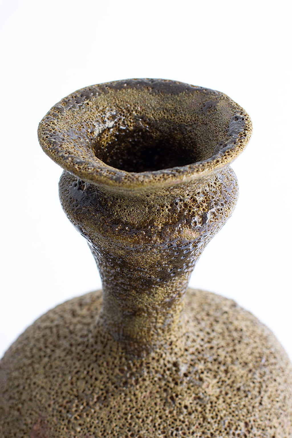 Canoa Lab Arq 006 Musgo Vase, a handcrafted stoneware vase featuring a unique, highly porous volcanic texture in rich musgo green and earthy brown tones with a subtly glossy finish. Its organic, brutalist-inspired silhouette with a flared mouth and constricted neck makes it a striking statement piece. Perfect for rustic shelf styling, organic modern interiors, or as a distinctive decorative vase for living rooms and entryways.