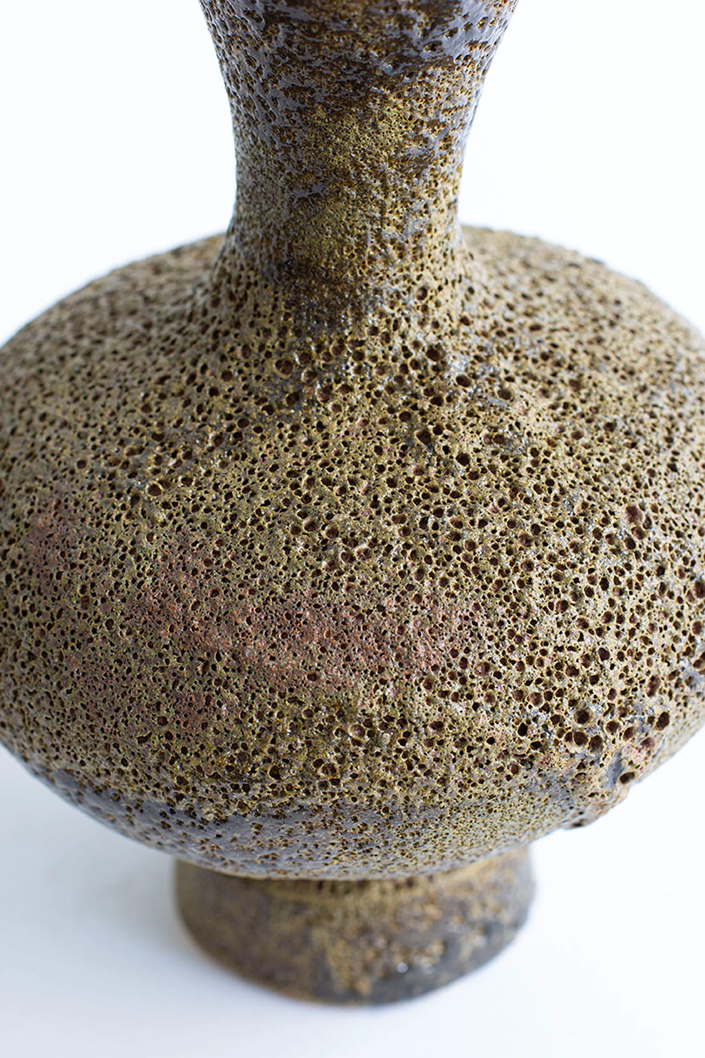 Canoa Lab Arq 006 Musgo Vase, a handcrafted ceramic vase with a distinct porous volcanic texture and an organic moss green and earthy brown glaze, featuring a globular body and narrow neck. This sculptural stoneware vase showcases varied dark brown and subtle reddish-brown hues, creating a rustic, brutalist aesthetic. Ideal for organic modern shelf styling or as a unique decorative accent in contemporary living rooms.