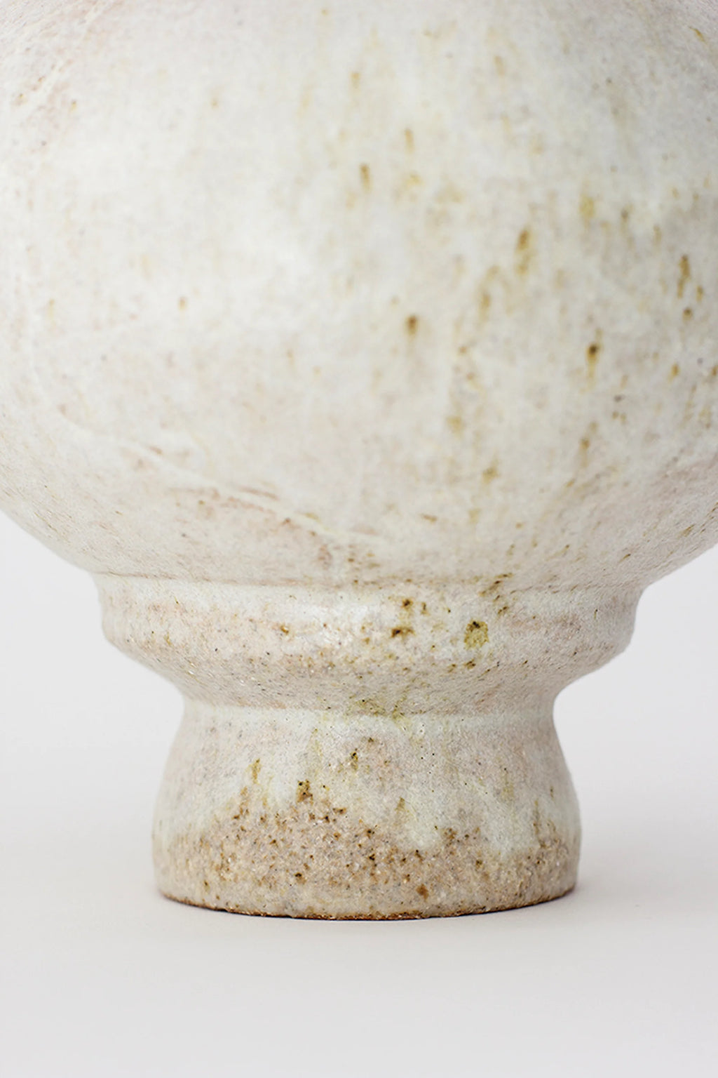 Canoa Lab Arq 007 Vase, a close-up detail of the speckled, off-white ceramic vase, highlighting its textured surface and the organic, handcrafted details of its pedestal base, on a white background.