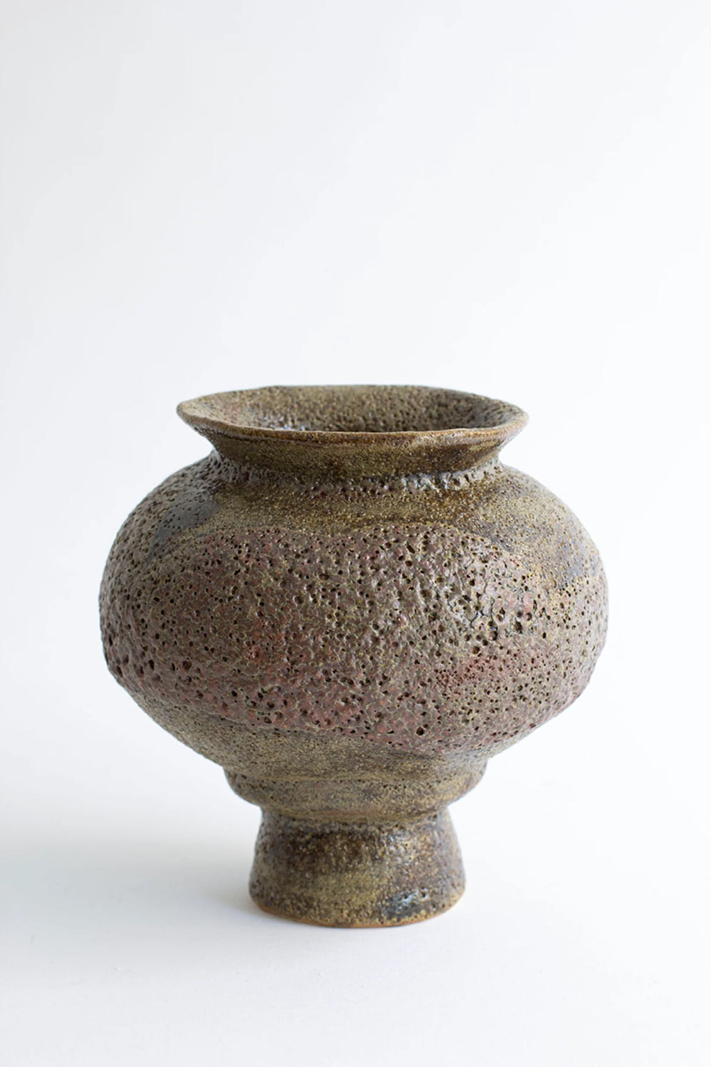 Canoa Lab Arq 007 Musgo Vase, a full view of the rustic, handcrafted ceramic vase with a textured, porous surface in earthy brown and green tones, featuring a rounded body and narrow neck, on a white background.