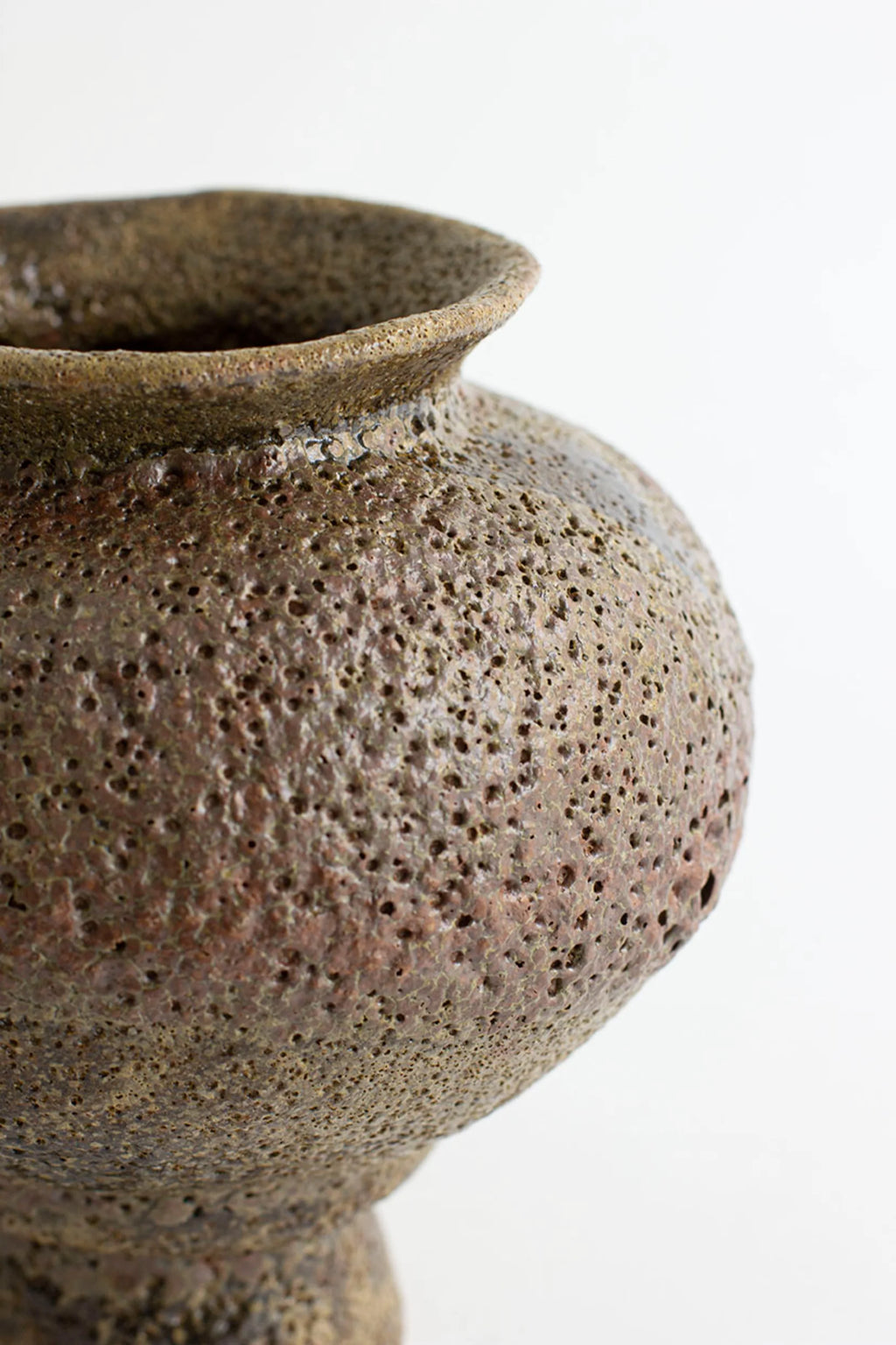 Canoa Lab Arq 007 Musgo Vase, a close-up of the rustic, handcrafted ceramic vase, highlighting its deeply textured, porous surface in rich earthy brown and green hues, on a white background.