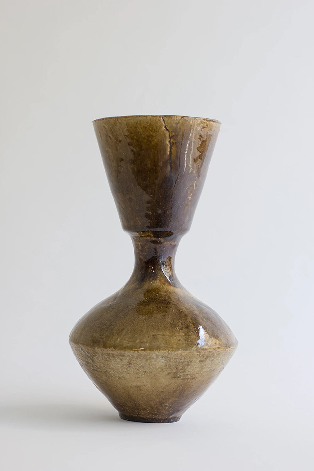 Canoa Lab Arq 008 Vase, a handcrafted ceramic vase with an organic, sculptural hourglass silhouette, featuring rich earthy brown and olive green glazes with a textured, rustic finish. This artisanal stoneware piece showcases a wide flaring mouth, narrow waist, and bulbous base, perfect for organic modern shelf styling or as a distinctive wabi-sabi living room accent.