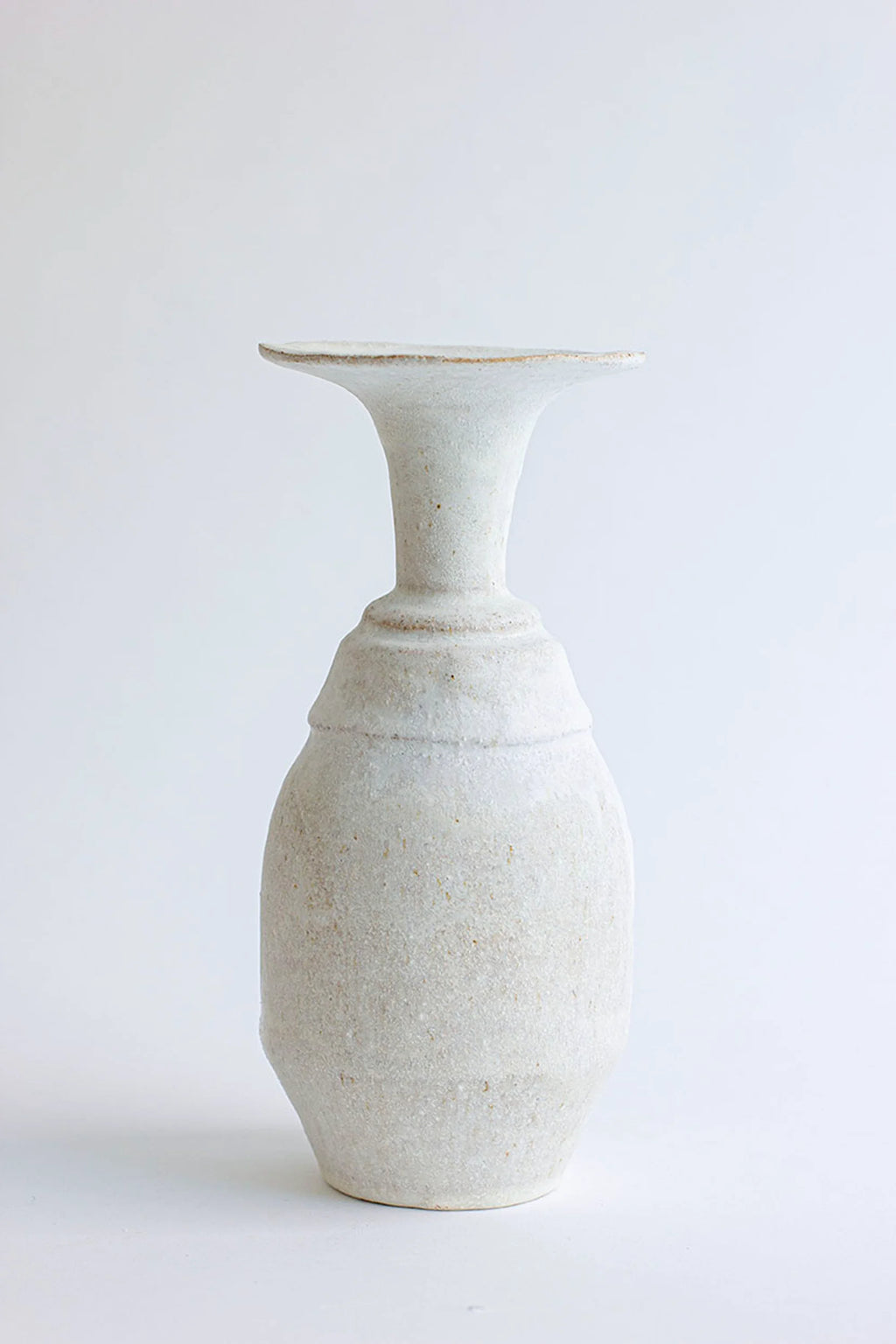 Canoa Lab Arq 011 Vase, a handcrafted stoneware ceramic vase in a natural off-white and sandy beige tone with a distinctive textured, porous finish. Its sculptural form features a flared rim, a narrow, tiered neck, and a full, rounded body, embodying an organic modern aesthetic. Perfect for wabi-sabi shelf styling, minimalist home decor, or as a contemporary accent piece in living rooms and bedrooms.