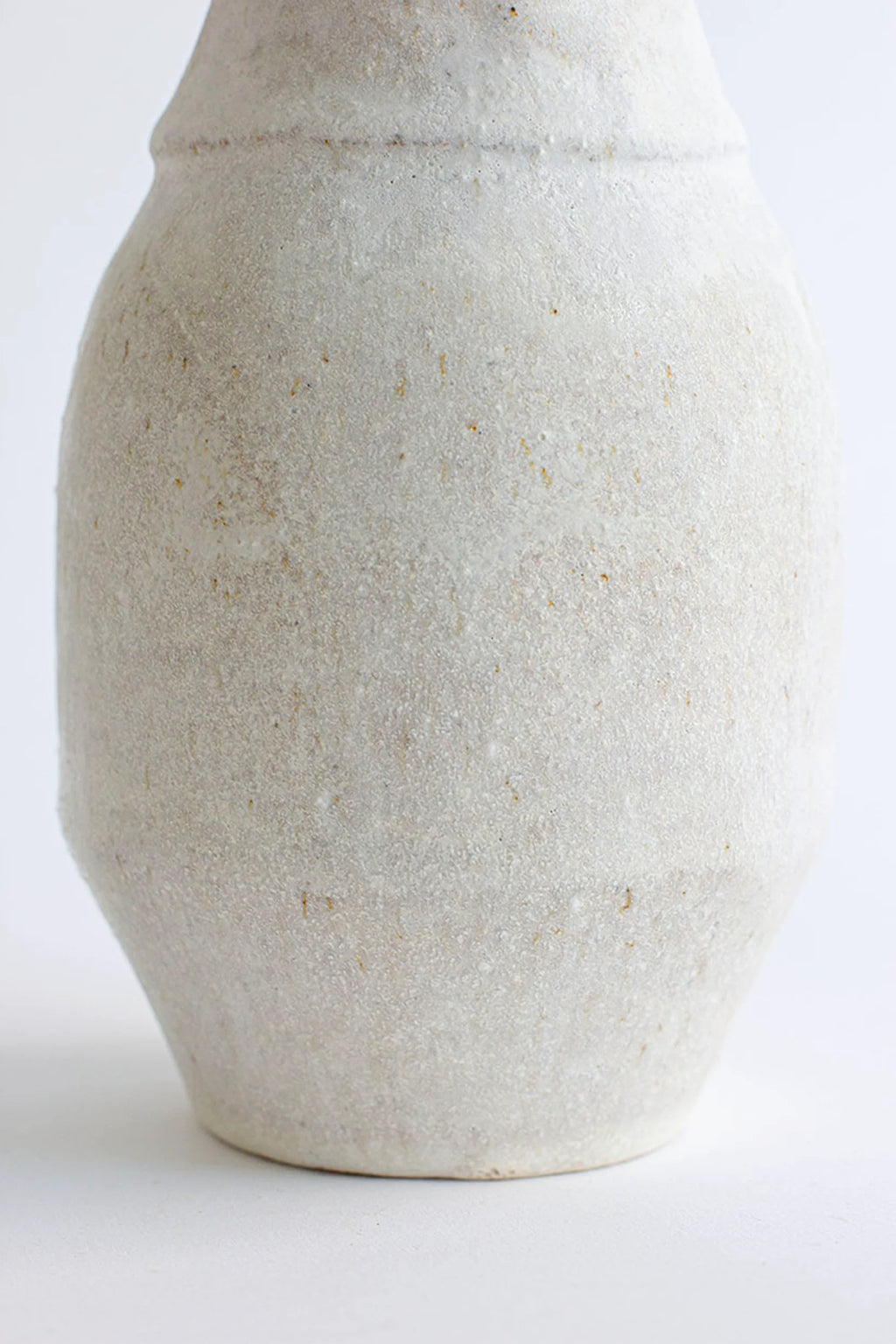 Canoa Lab Arq 011 Vase, a handcrafted organic modern ceramic vase in a warm cream color with a porous, sandy texture and subtle natural flecks. This minimalist stoneware vase features a gently curved cylindrical body and a distinct horizontal ridge, perfect for wabi-sabi or rustic shelf styling in living rooms or bedrooms.
