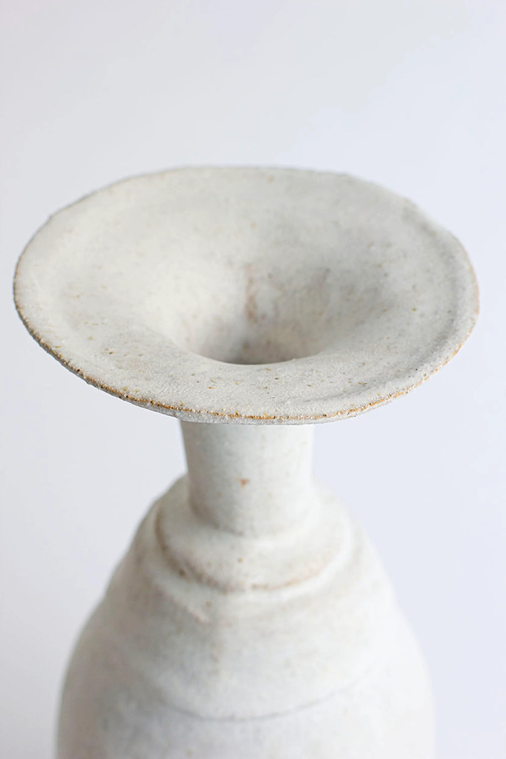 Canoa Lab Arq 011 Vase, a handcrafted stoneware vase featuring a wide, flared organic mouth and a textured, porous off-white finish, showcasing natural sand-colored speckles and an unglazed, rustic minimalist aesthetic. This contemporary ceramic art piece is ideal for organic modern shelf styling or as a unique dining table centerpiece.