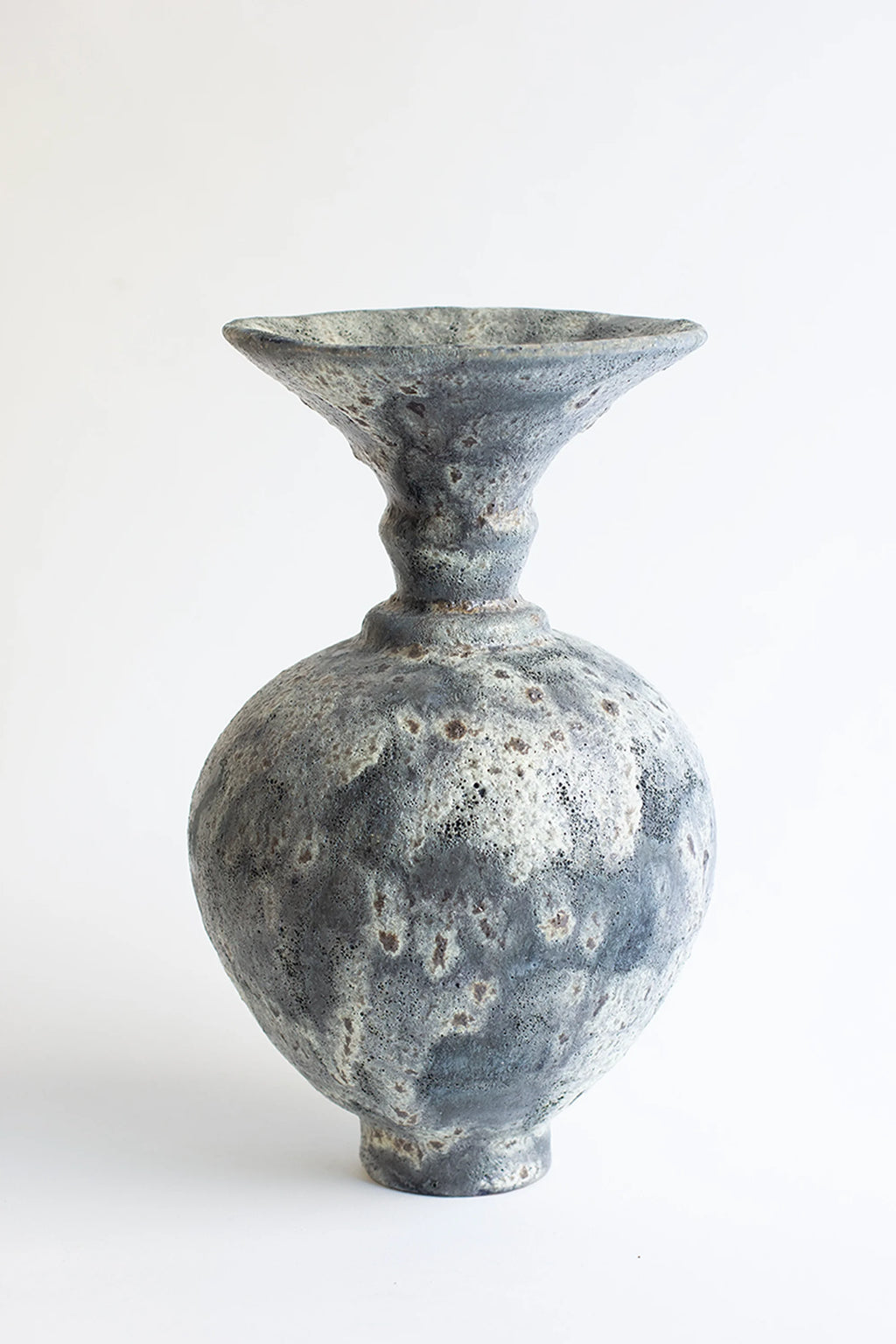 Canoa Lab Ánfora Gecko Vase, a handcrafted ceramic vase with a distinctive dark grey and off-white volcanic glaze, featuring a highly textured, porous surface and warm brown speckles. Its organic, bulbous body tapers to a narrow neck and a wide, flared rim, embodying a rustic, Brutalist aesthetic. This artisanal stoneware piece is perfect for organic modern shelf styling, wabi-sabi interiors, or as a striking decorative vase for living rooms and entryways.